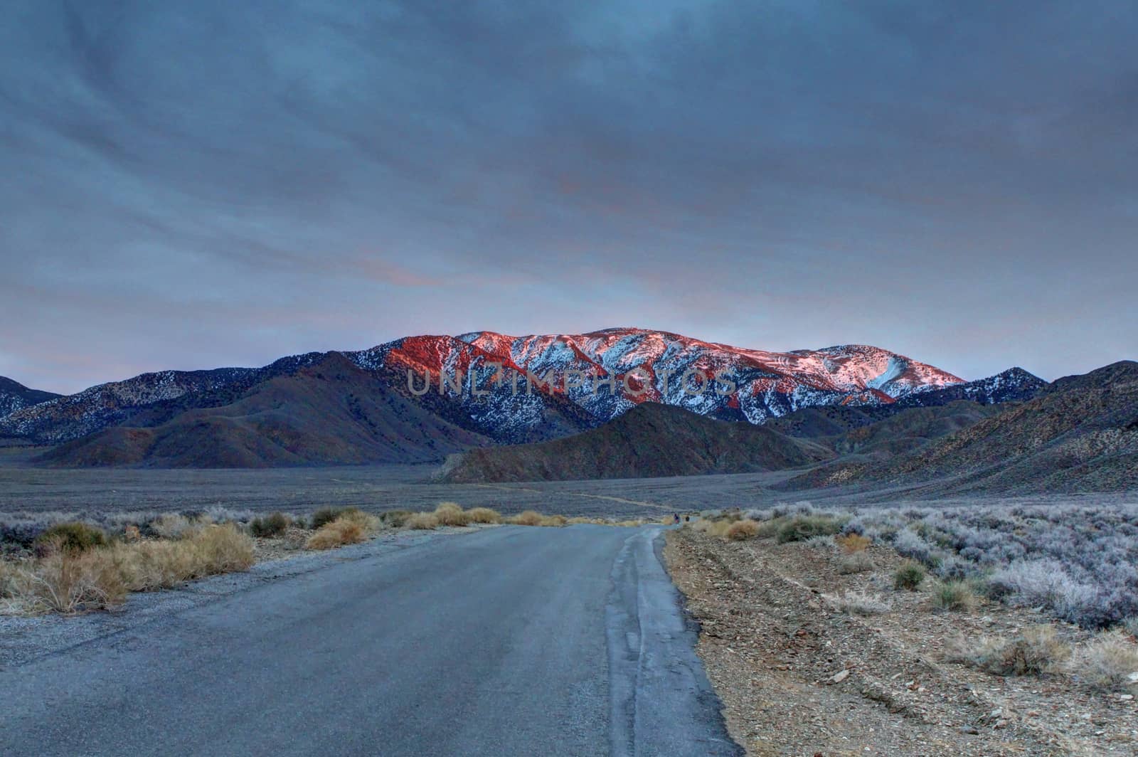 A lonely road toward a snow covered mountain in the desert.