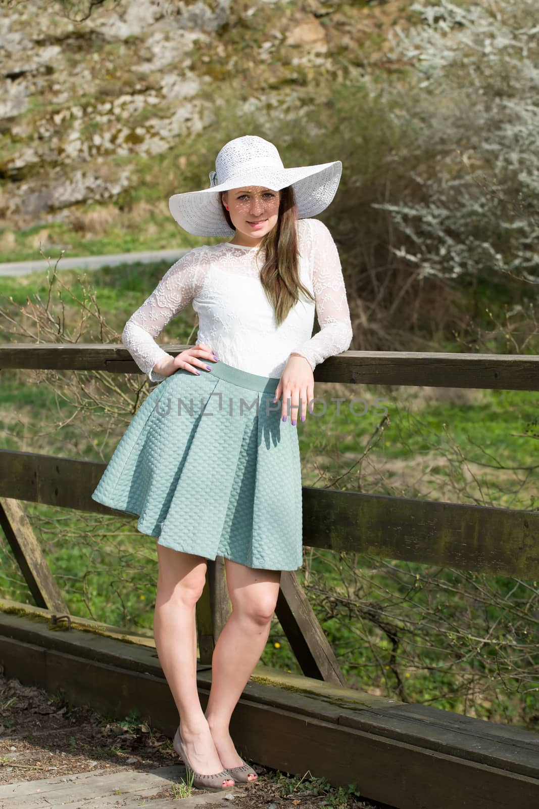 Cheerful fashionable woman in stylish hat and frock posing outdoor. Happy brunette girl with long hair in warm spring day