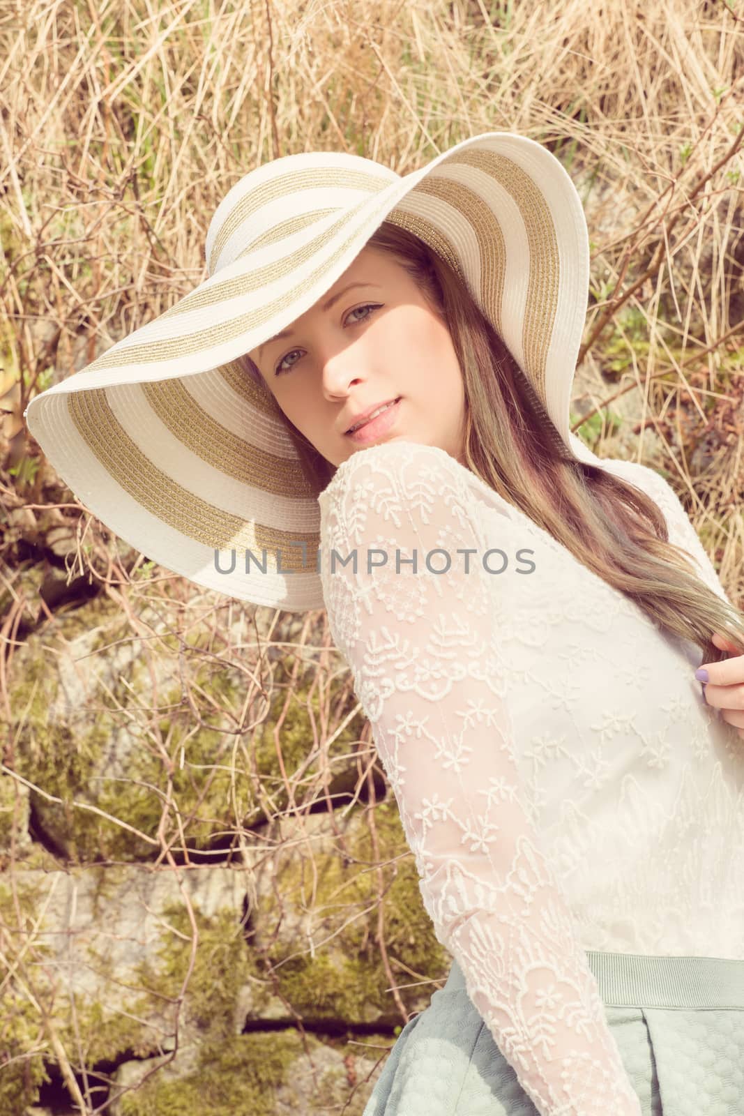Cheerful fashionable woman in stylish hat and frock posing outdoor. Happy brunette girl with long hair in warm spring day