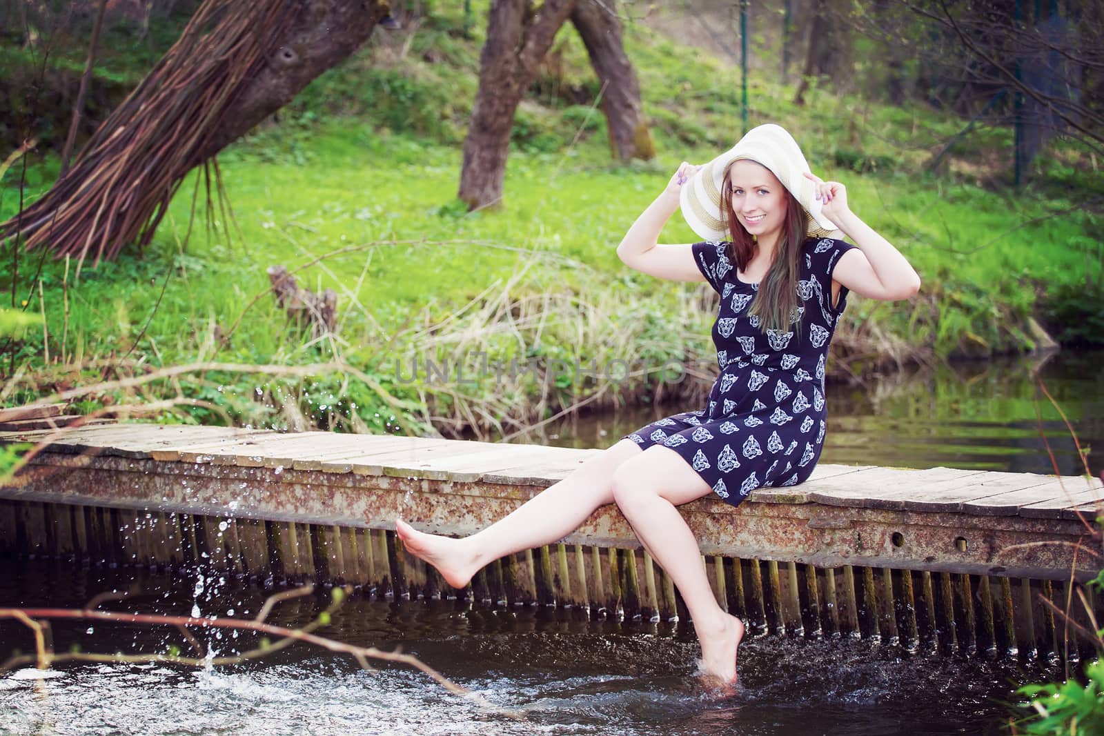Cheerful fashionable woman sits on small bridge and splashing wa by artush