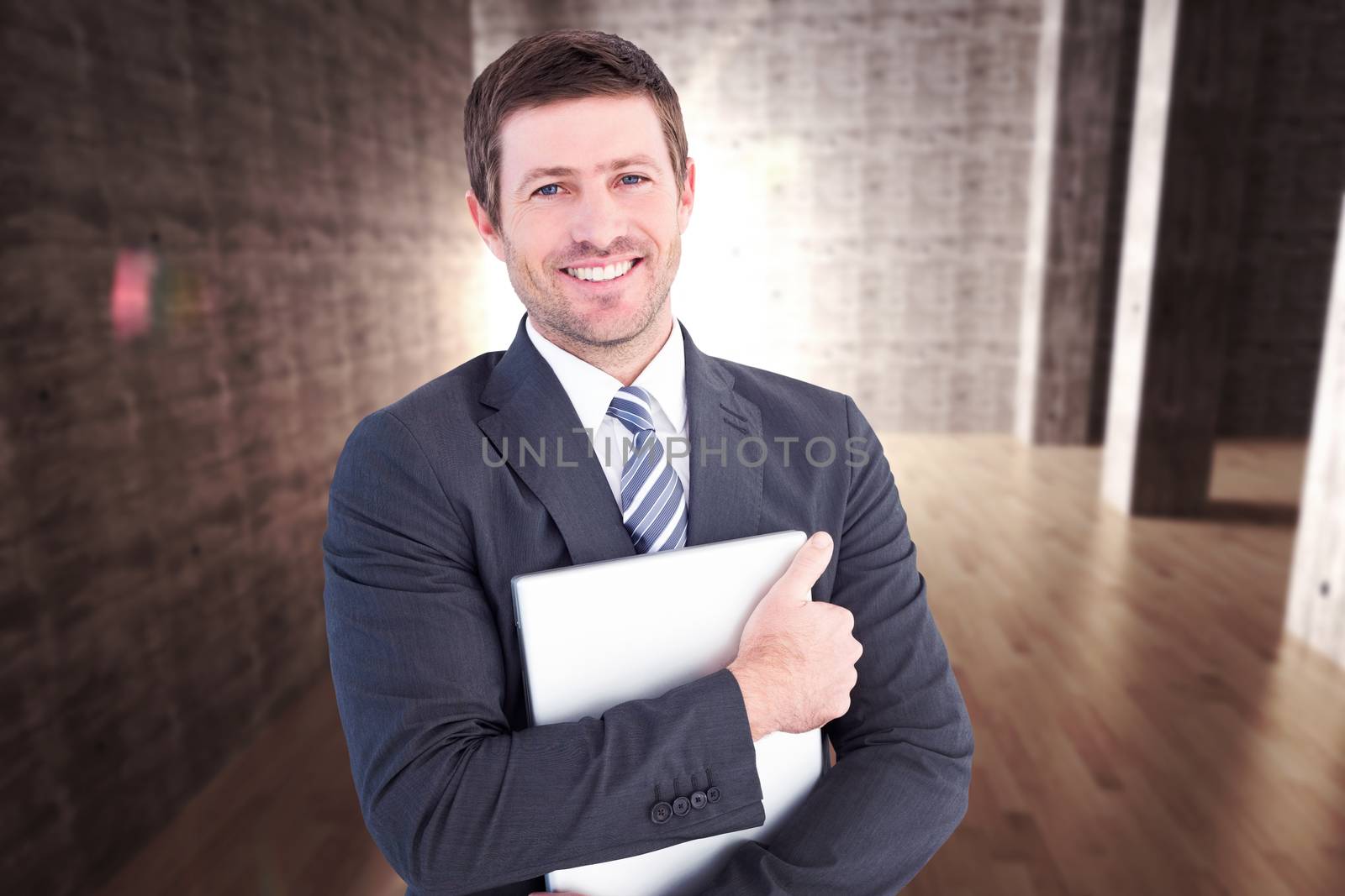 Businessman holding his laptop tightly against abstract room