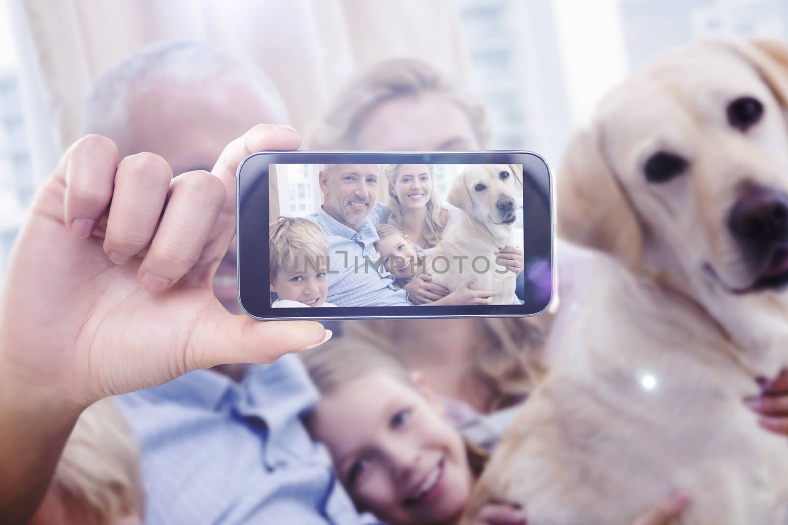 Hand holding smartphone showing against parents and their children on sofa with labrador