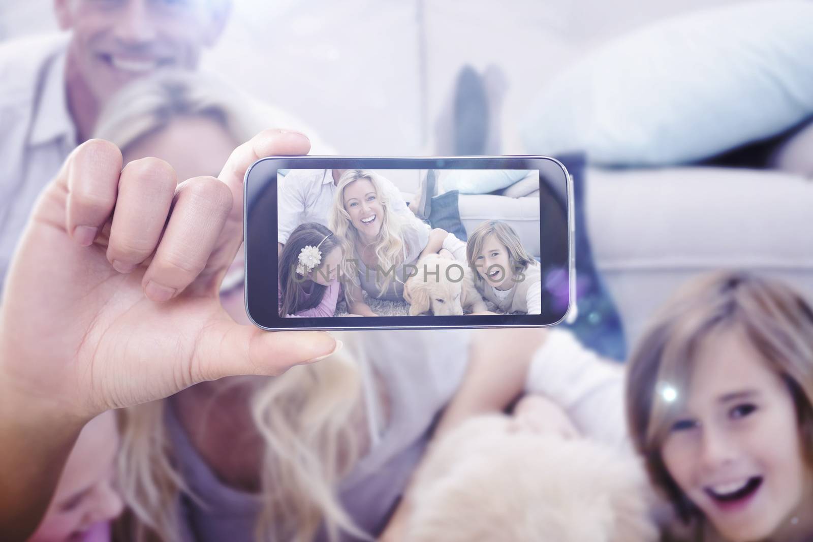 Hand holding smartphone showing against laughting family with their pet yellow labrador on the rug