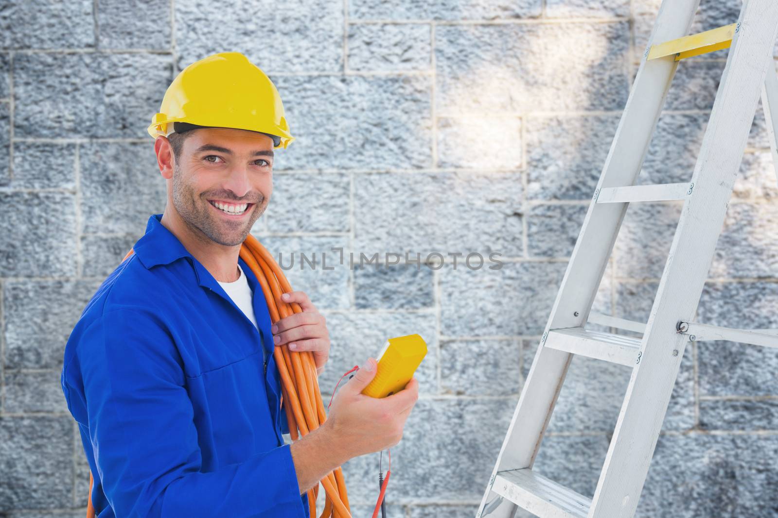 Smiling male electrician holding multimeter in office against grey