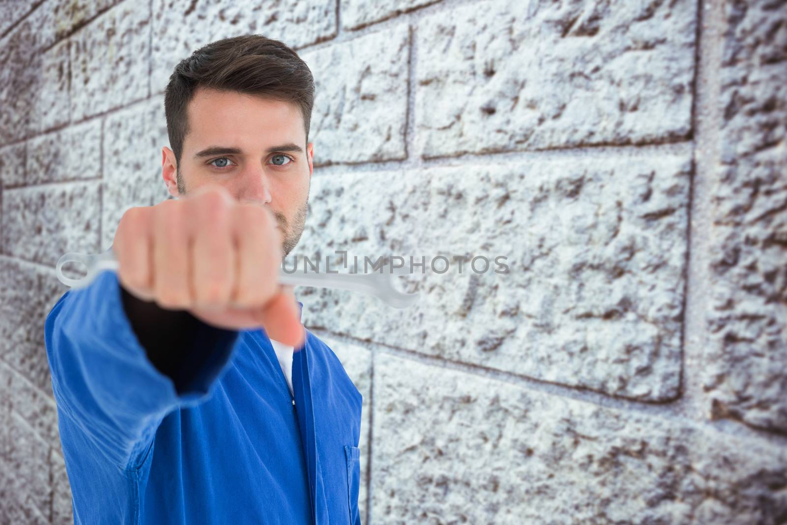 Confident young male mechanic holding spanner against grey brick wall