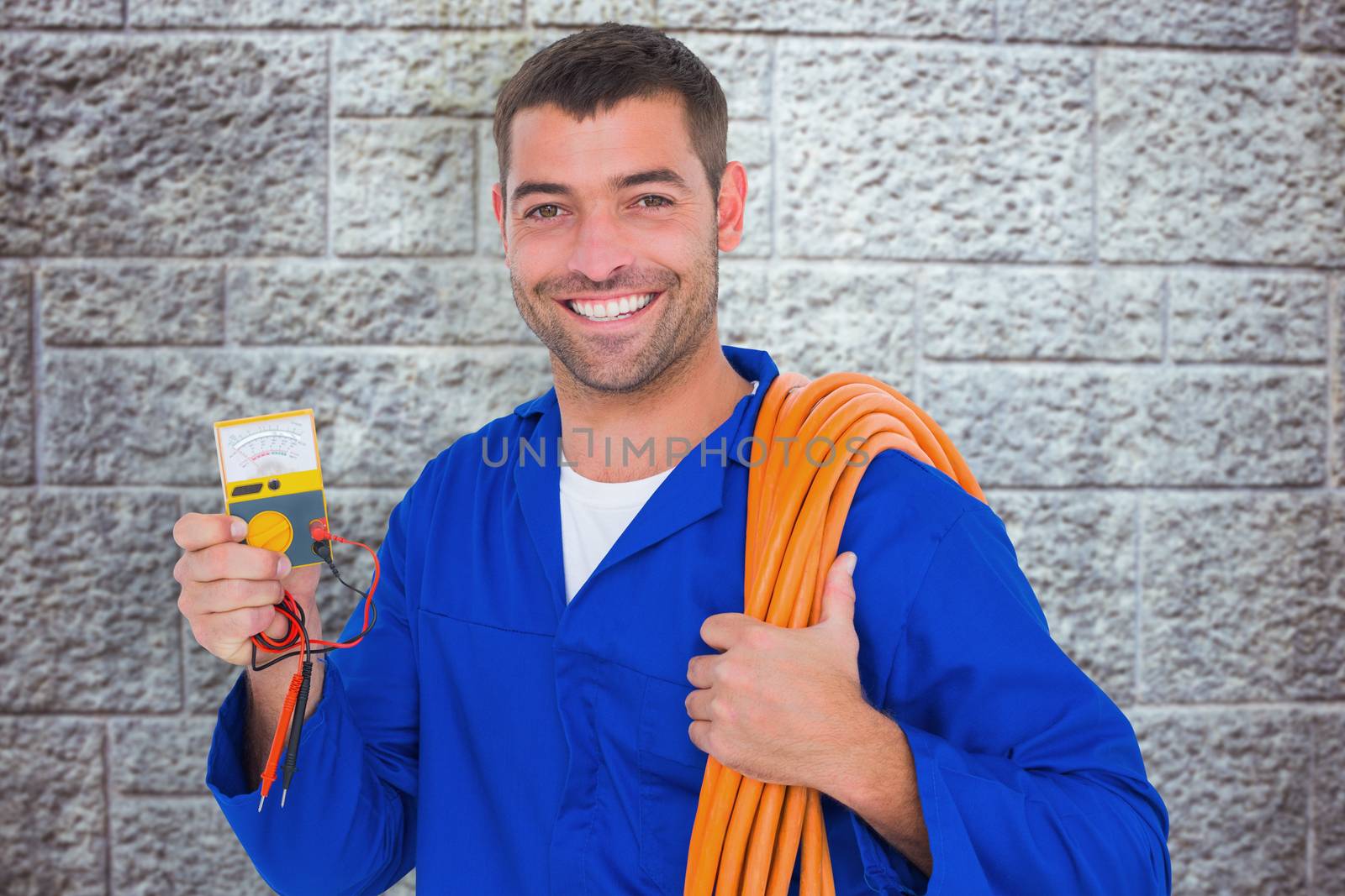 Smiling electrician with rolled wire and multimeter against grey brick wall