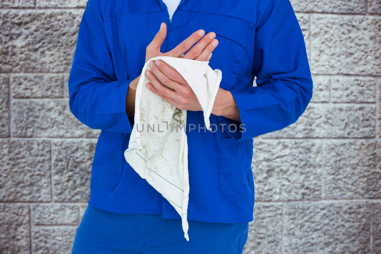 Cropped image of mechanic wiping hand with napkin against grey brick wall