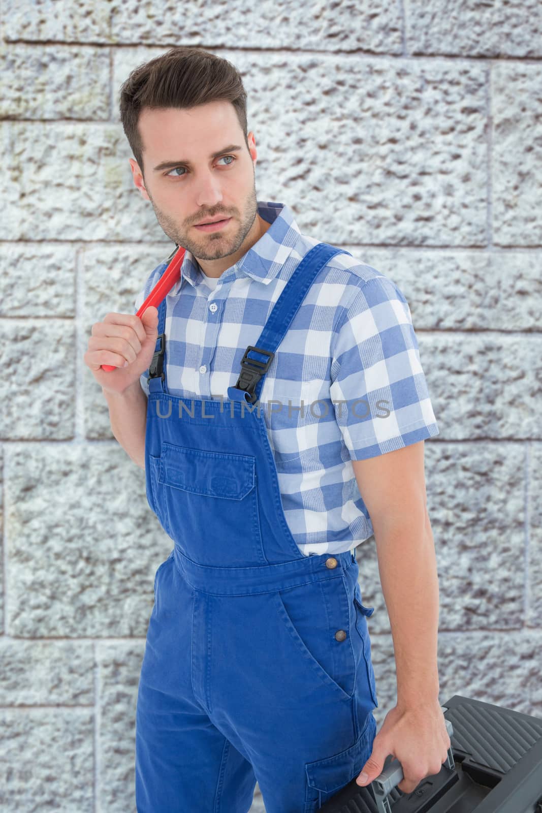 Repairman carrying toolbox while looking asway against grey brick wall