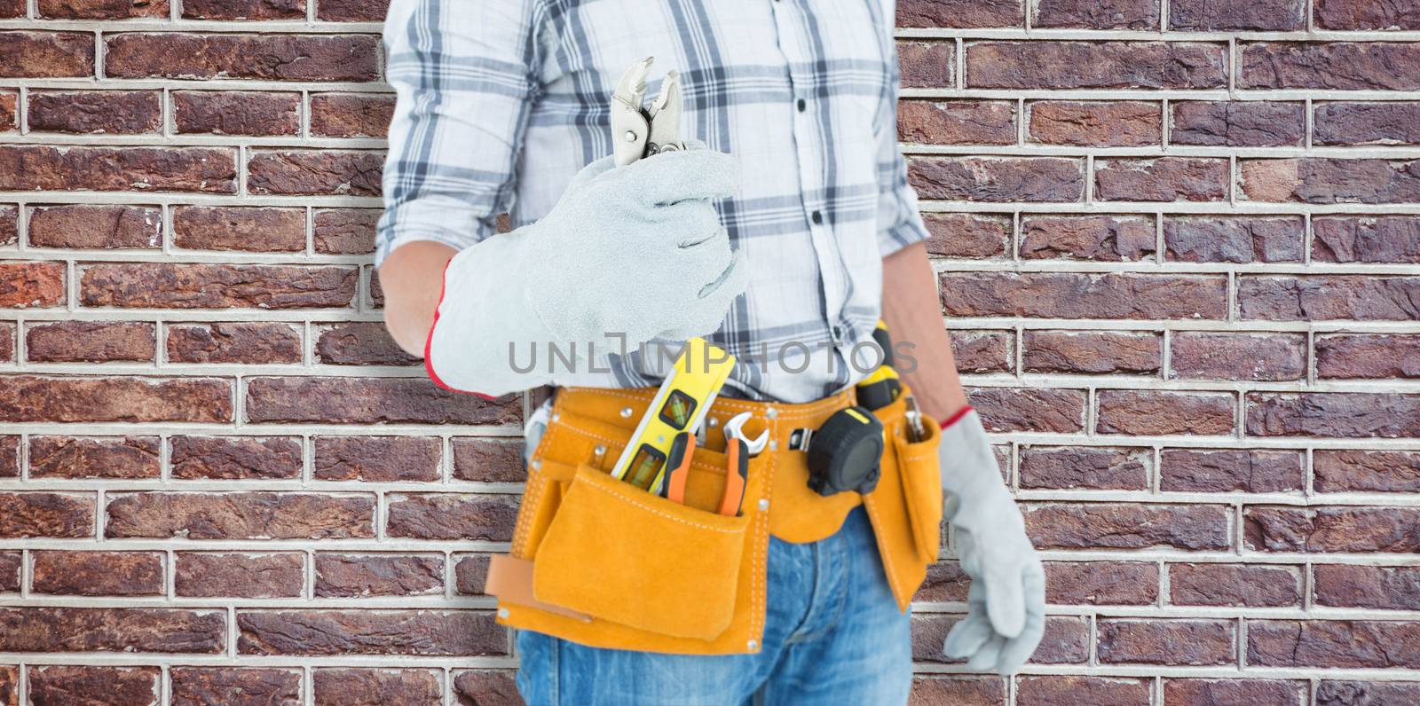 Technician with tool belt around waist holding pliers against red brick wall