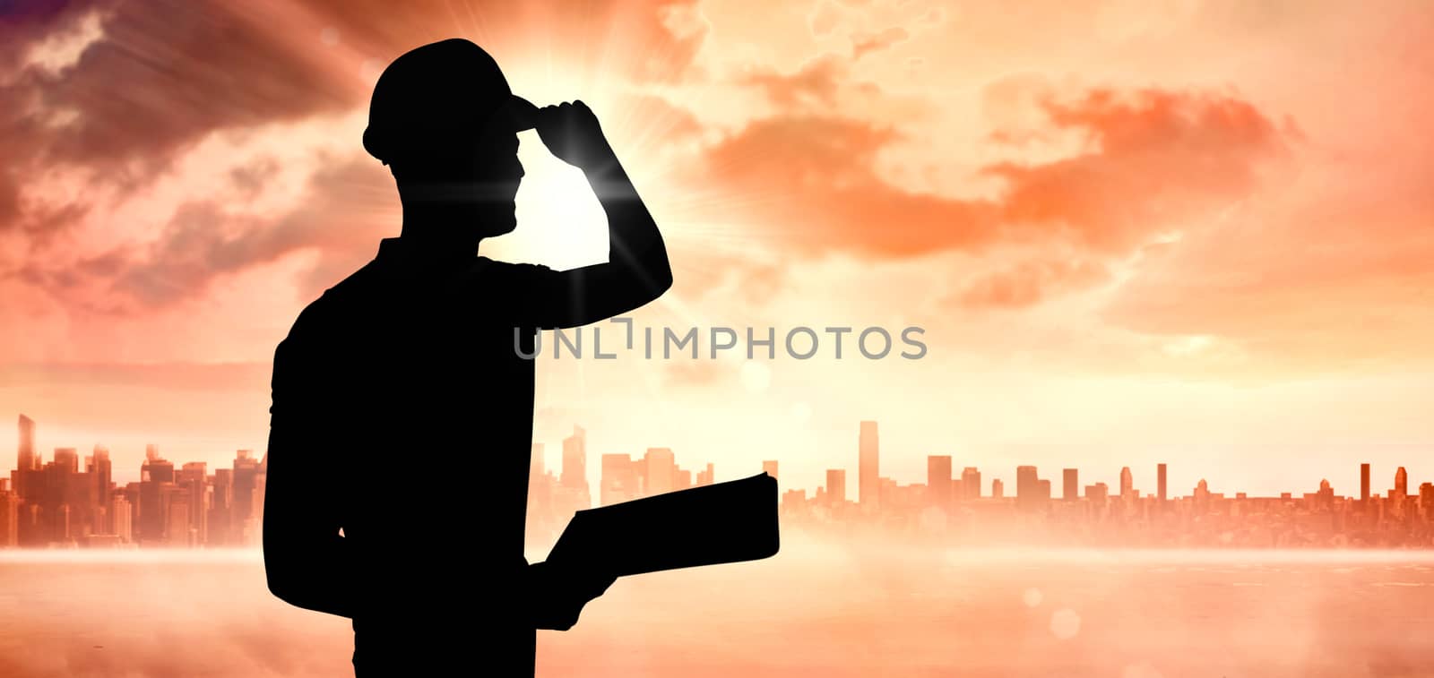 Manual worker wearing hardhat while holding clipboard against sun shining over city