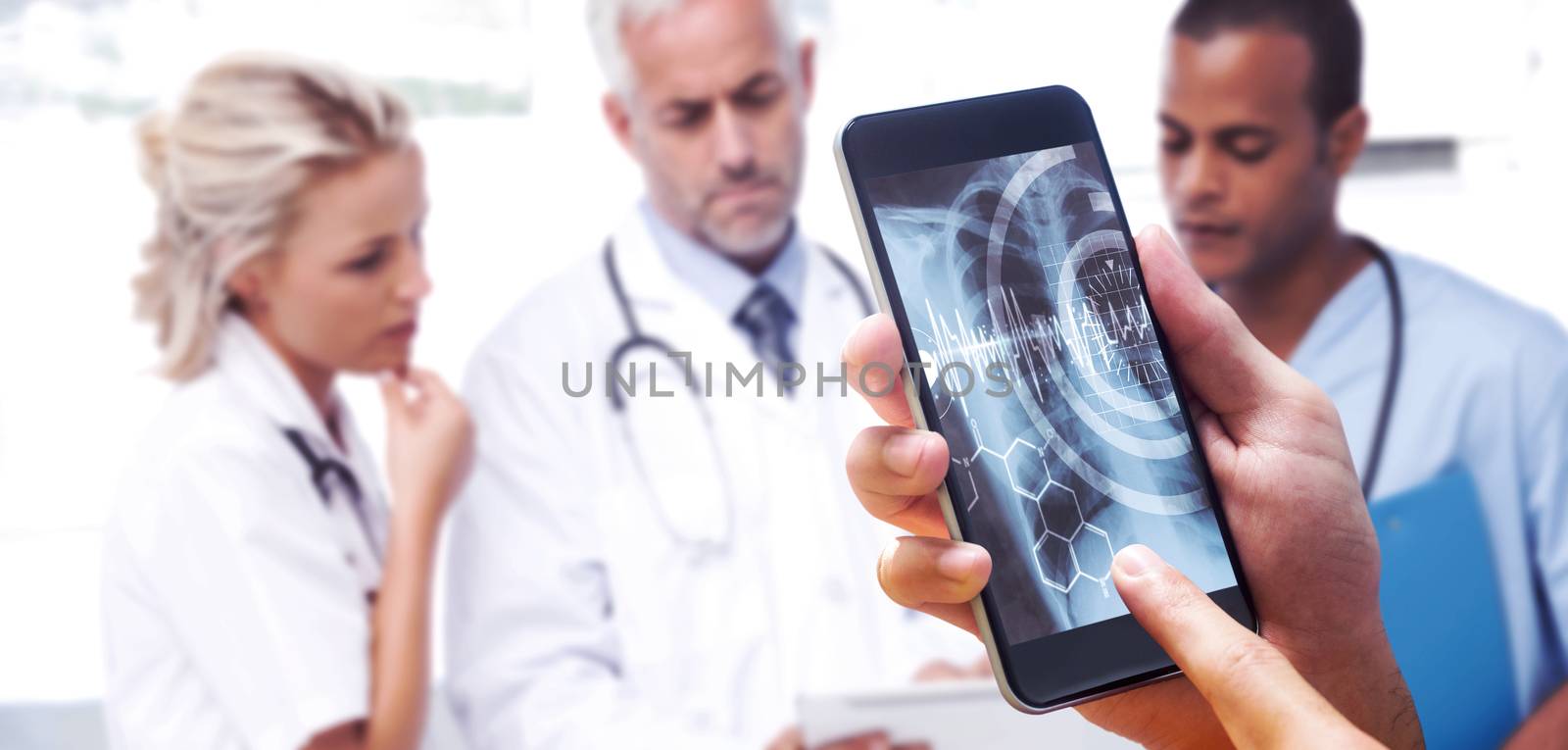 hand holding smartphone against three doctors using a tablet