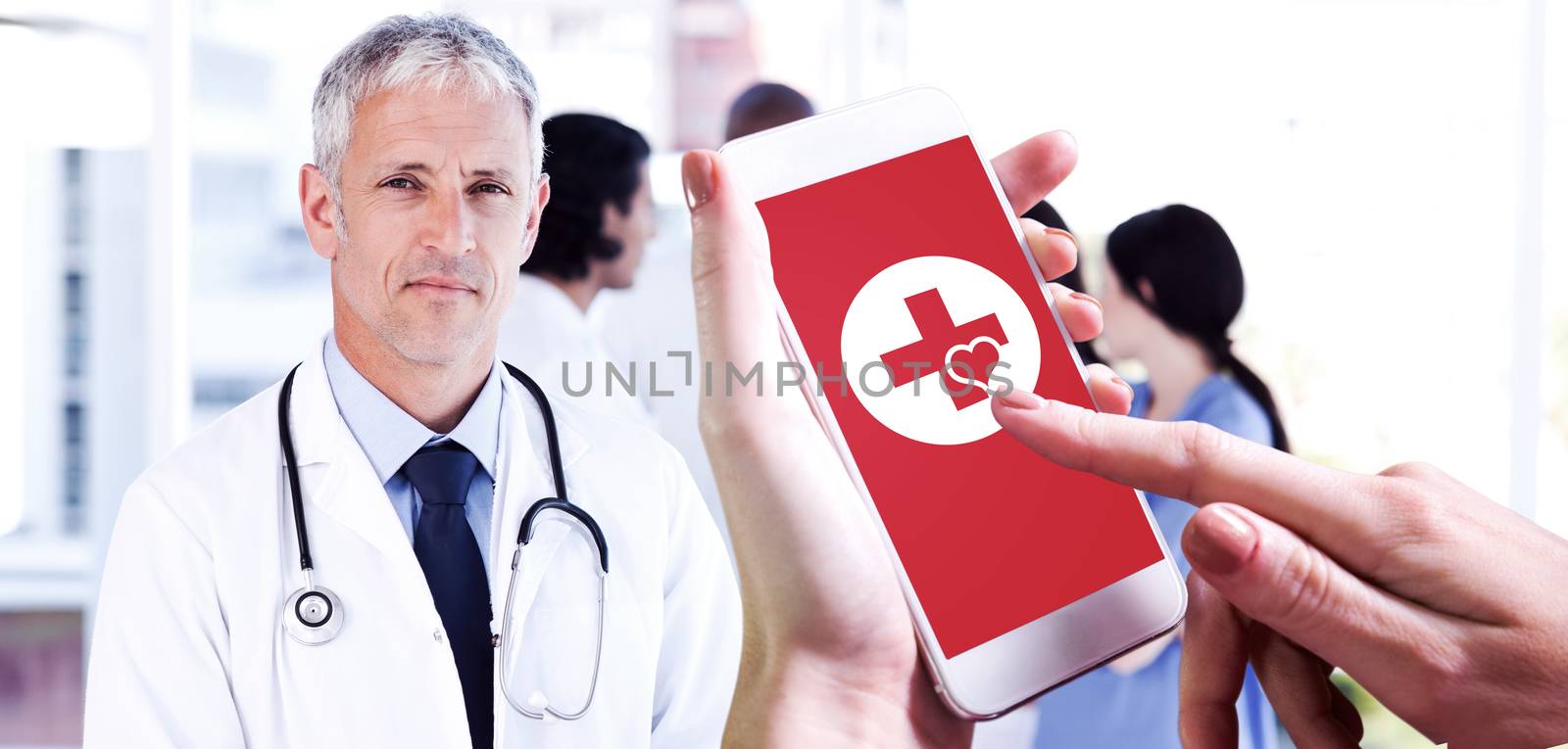 Hand holding smartphone against mature doctor pointing at something on his clipboard