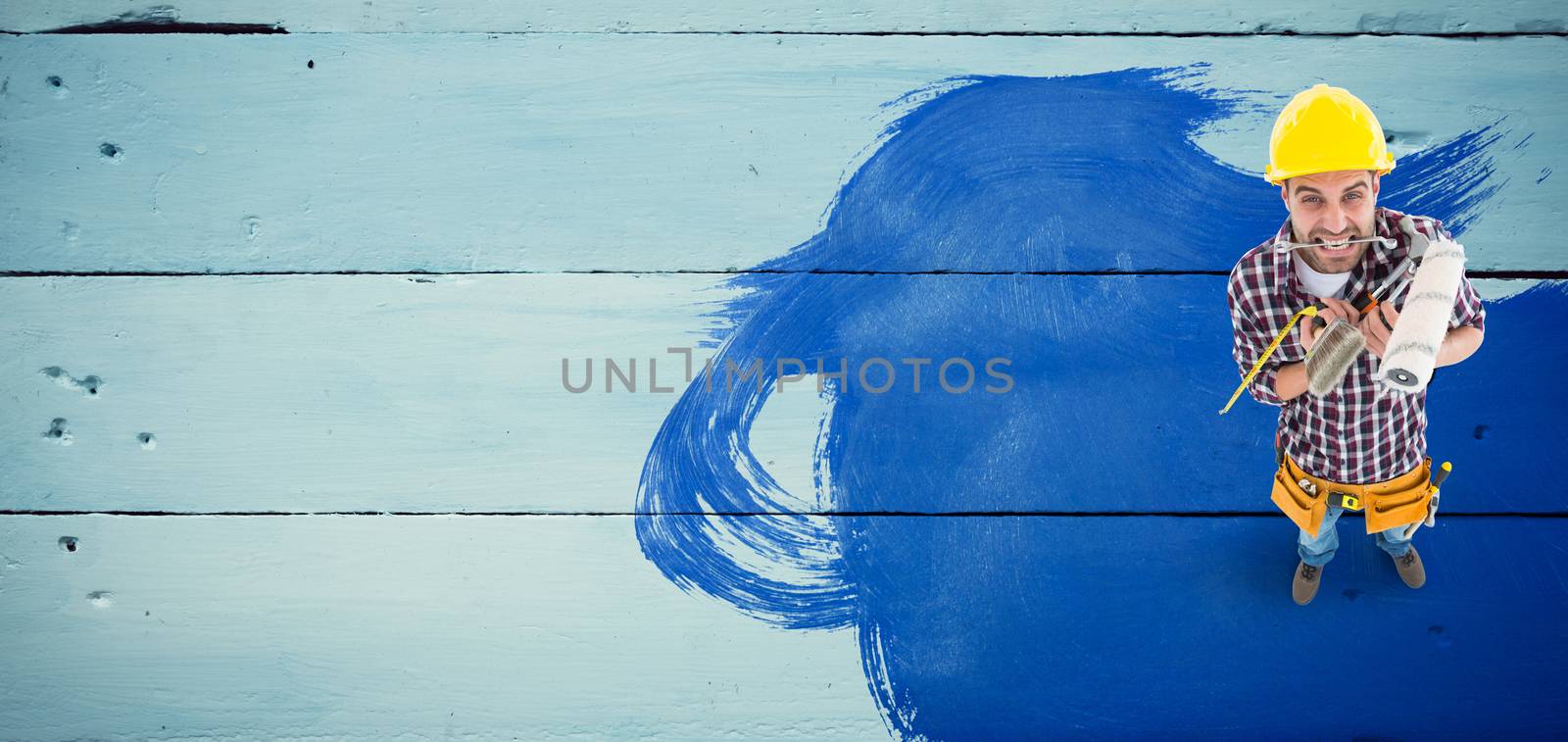 Frustrated handyman holding various tools against painted blue wooden planks