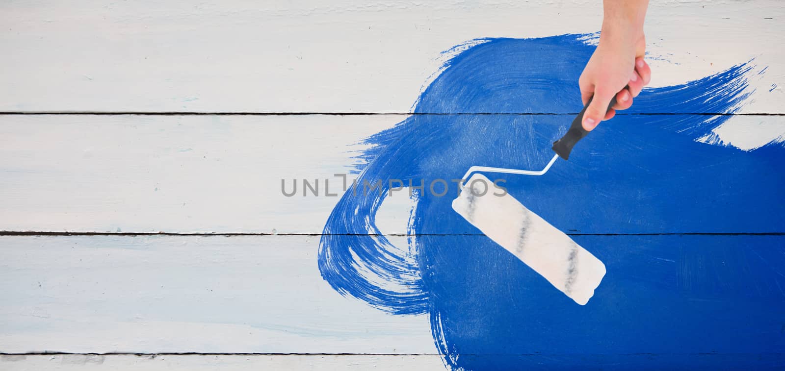Handyman holding paint roller  against painted blue wooden planks