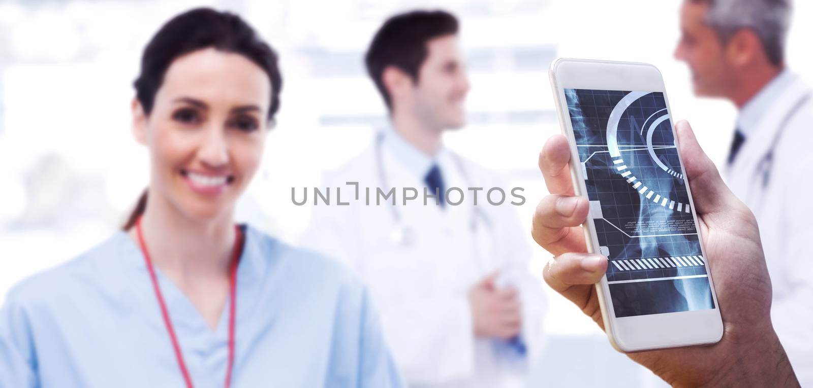 hand holding smartphone against nurse smiling at camera while doctors are talking together 