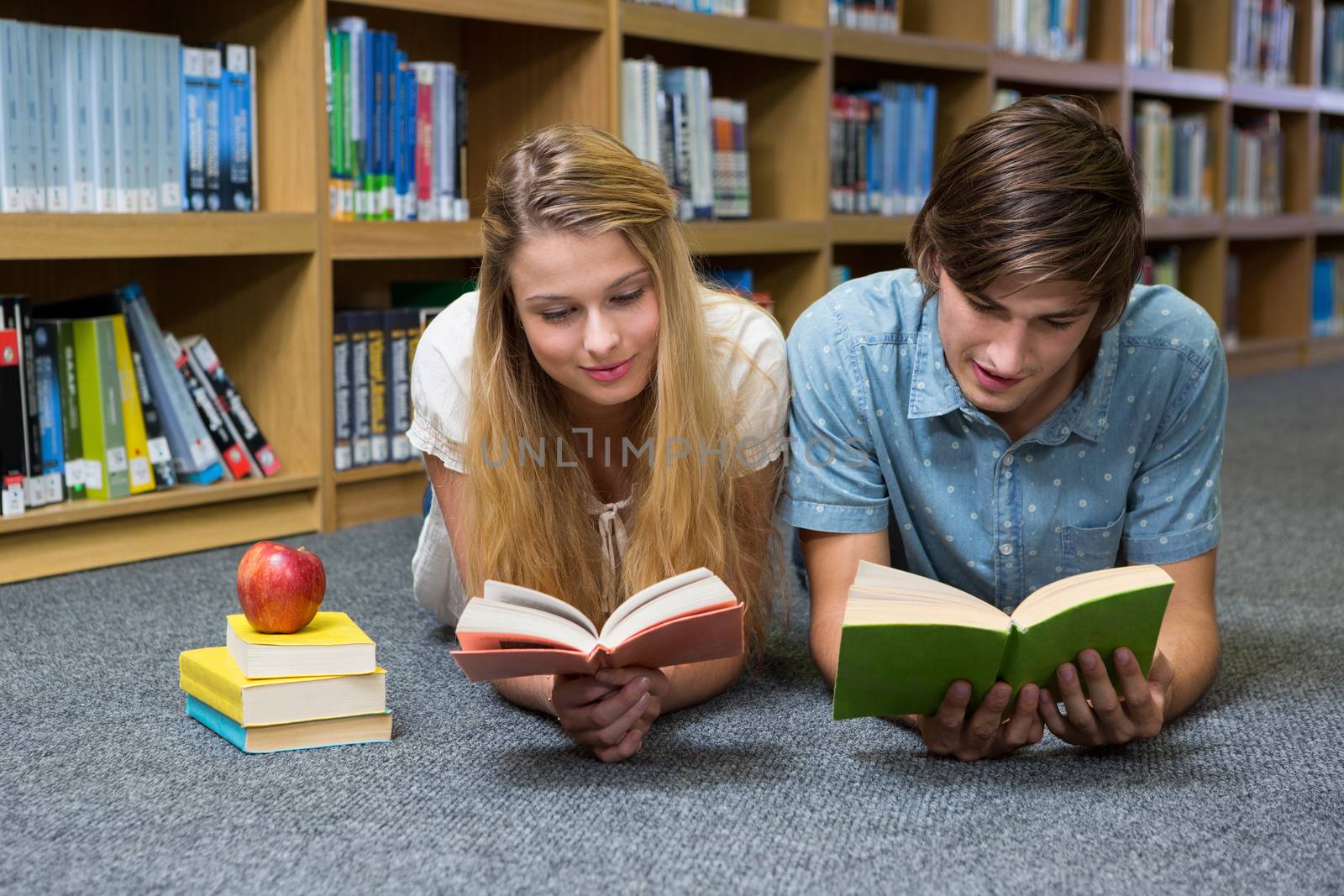 Students reading book lying on library floor at the university 