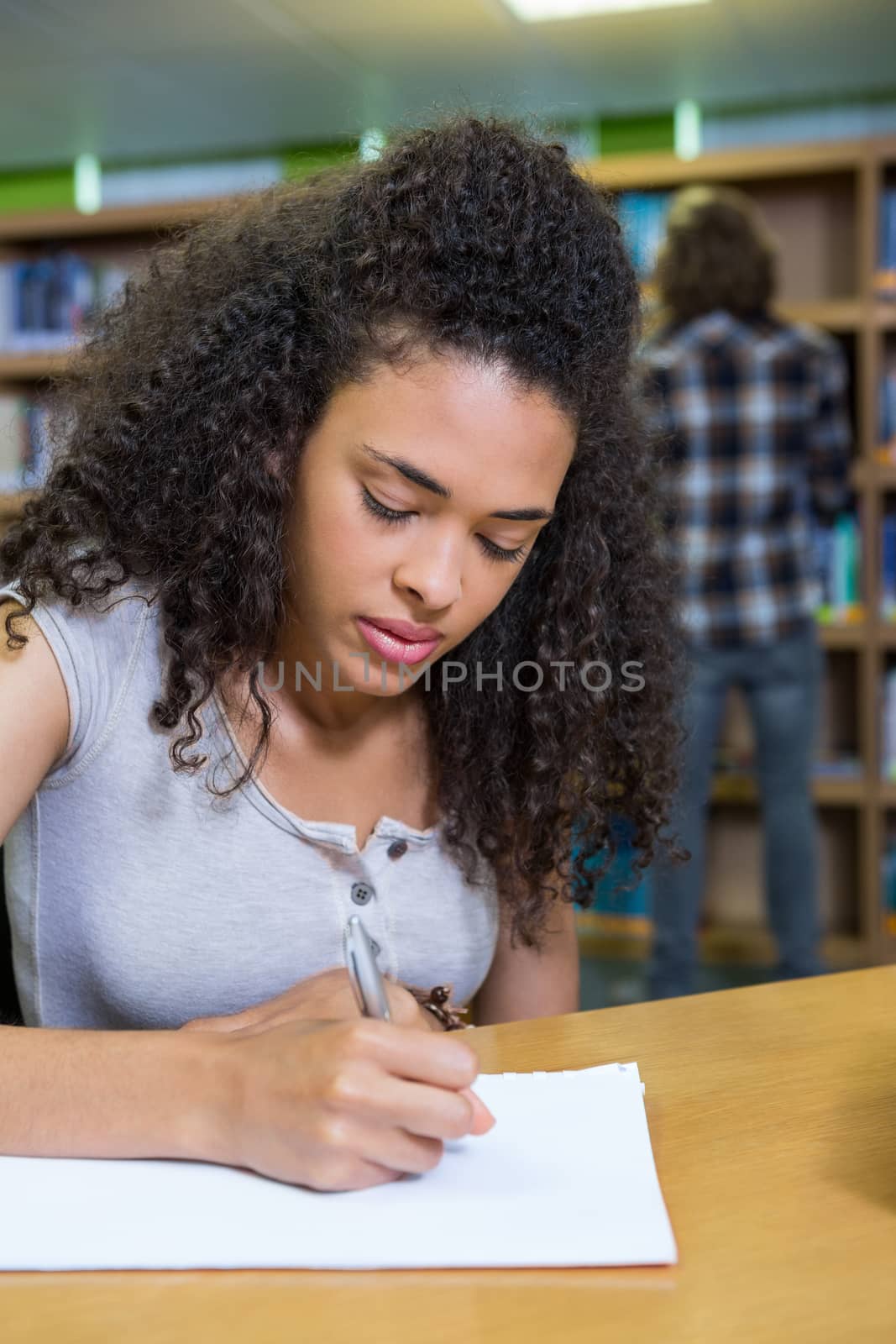 Student writing notes in notepad in the library at the university 