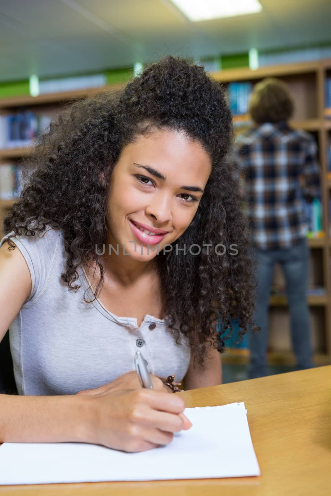 Student writing notes in notepad in the library at the university 