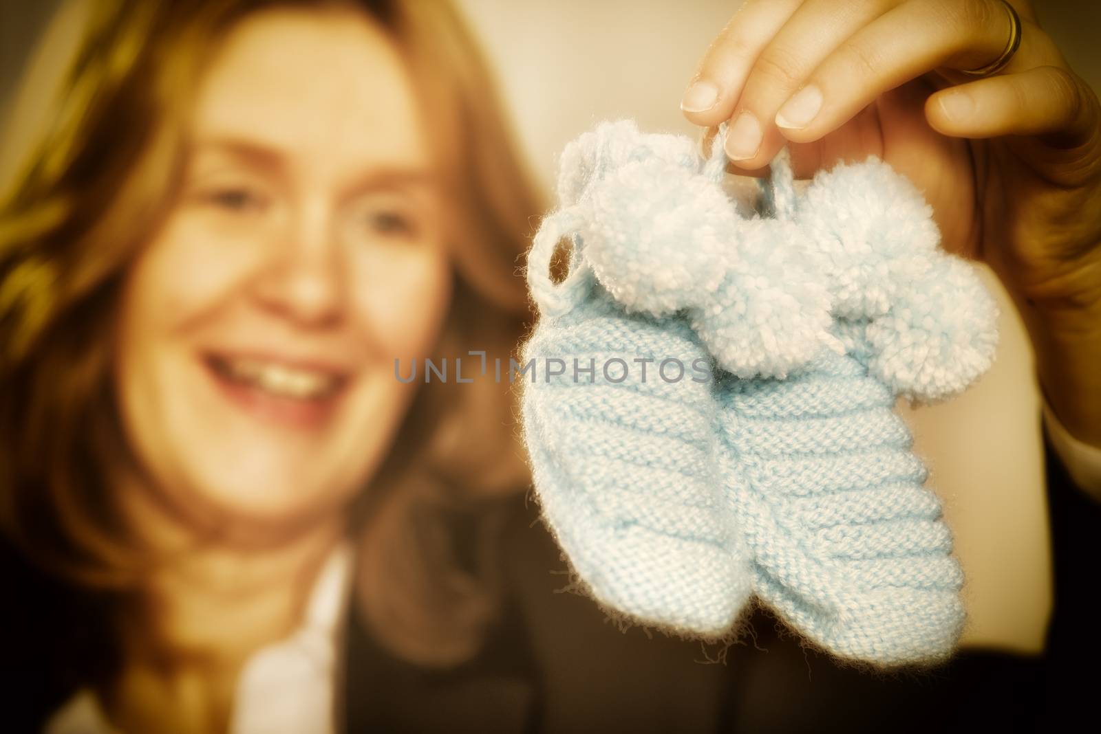 Blond woman is holding two blue baby shoes