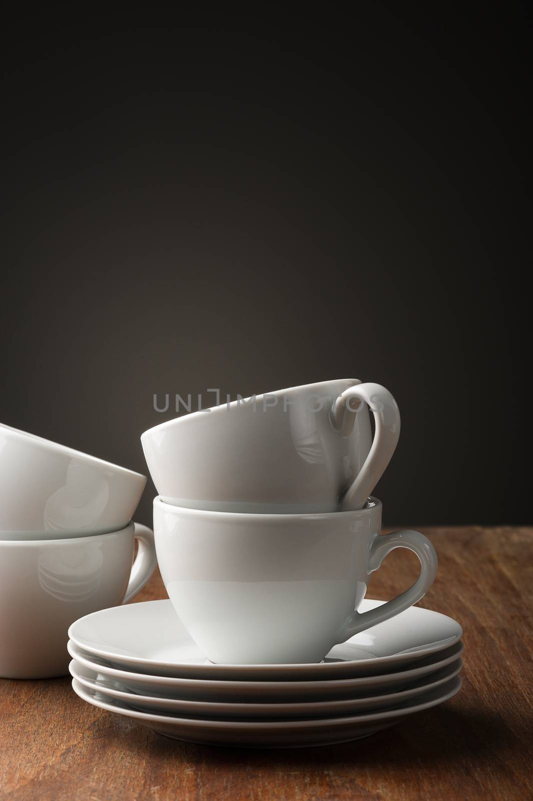 Two plain white pottery tea or coffee cups with stacked saucers standing ready on a wooden table to serve a relaxing cup of hot beverage, with vertical copyspace