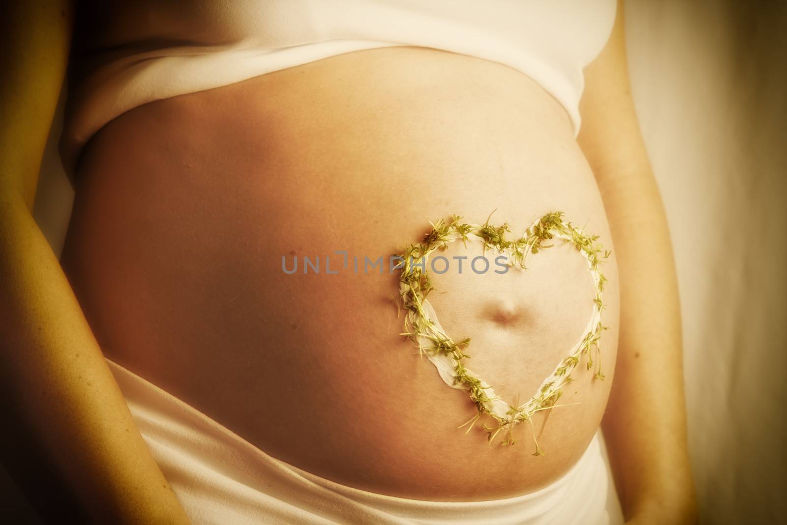 Image of a baby bump with cream cress heart in warm sun light