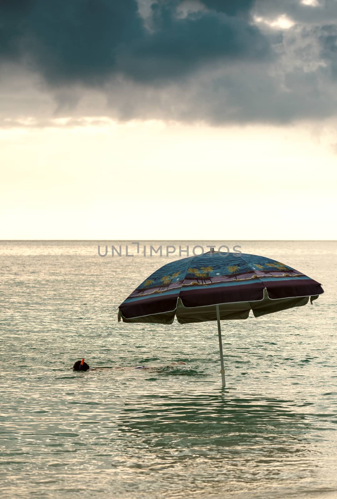 Snorkeling at sunset with beach umbrella in the ocean.