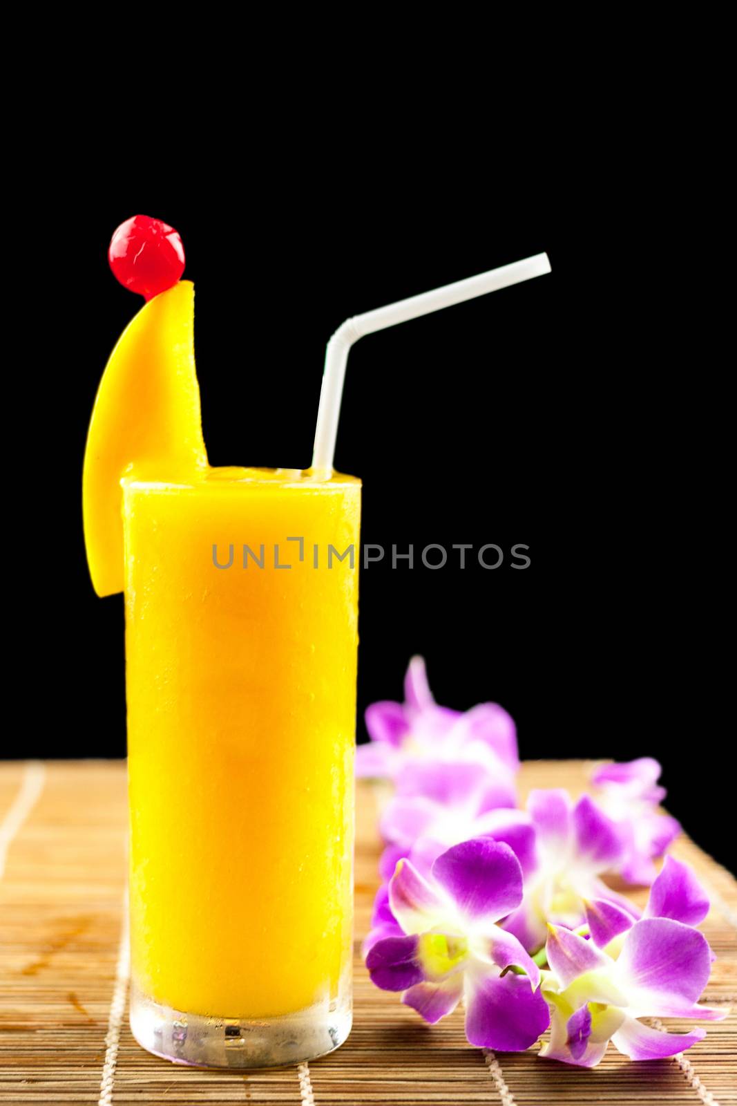 Mango juice and fruit on glass near beautiful flower isolation black background .
