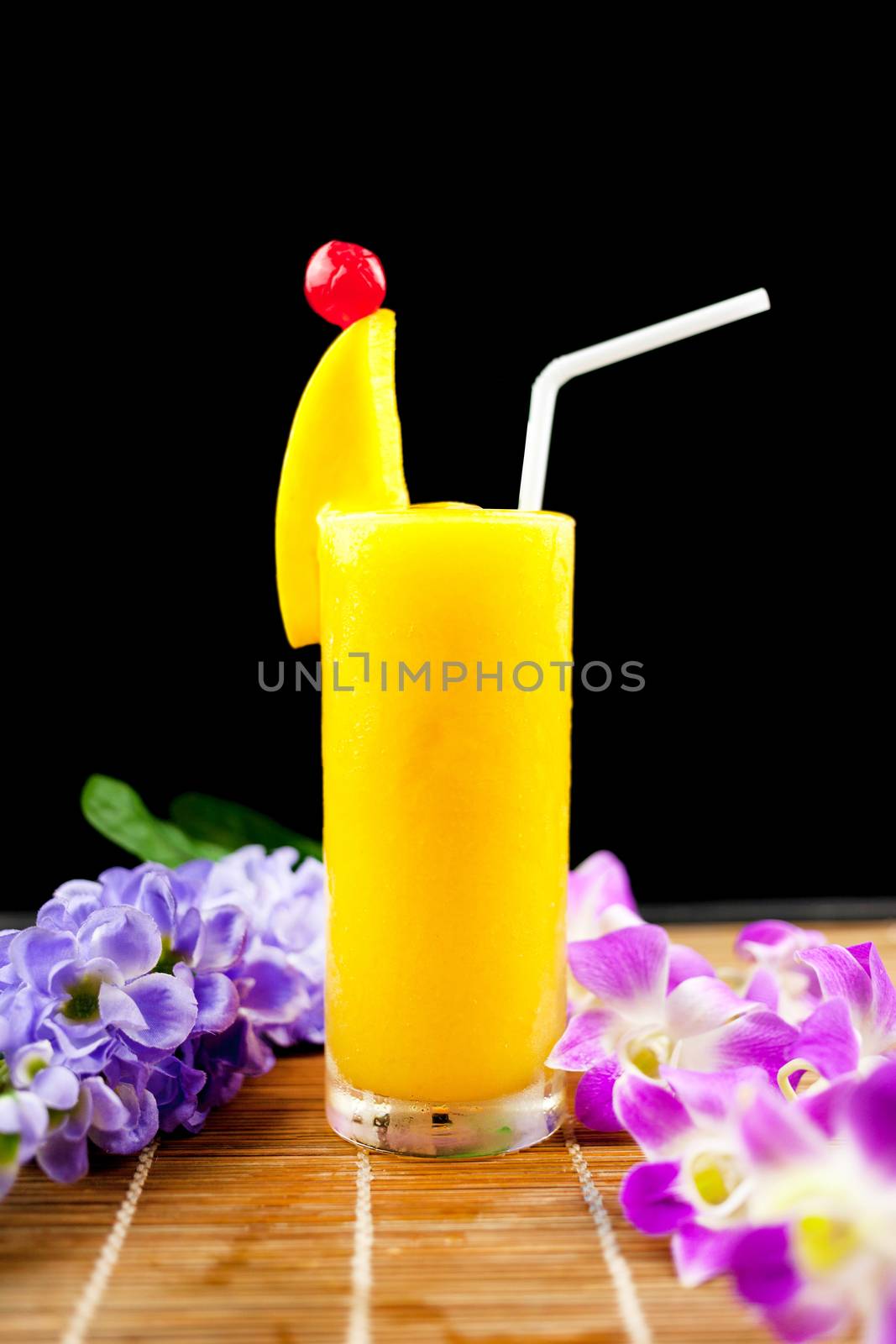 Mango juice and fruit on glass near beautiful flower isolation black background .