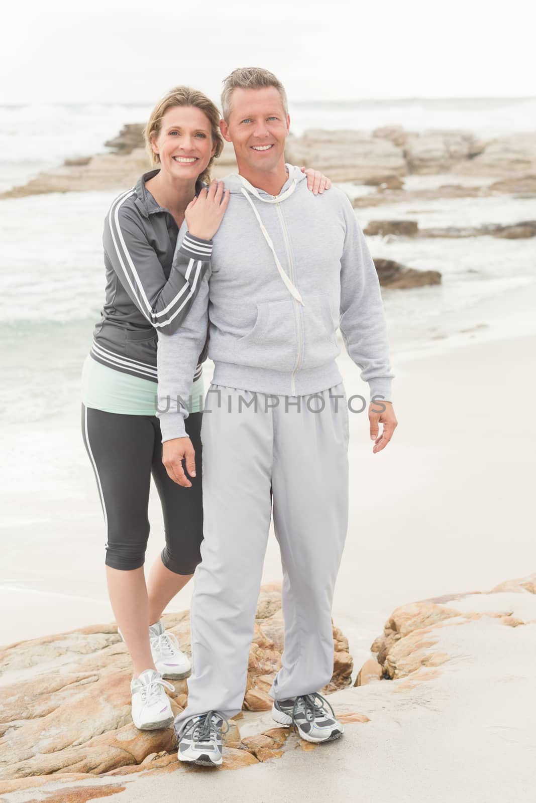 Fit couple smiling at camera at the beach