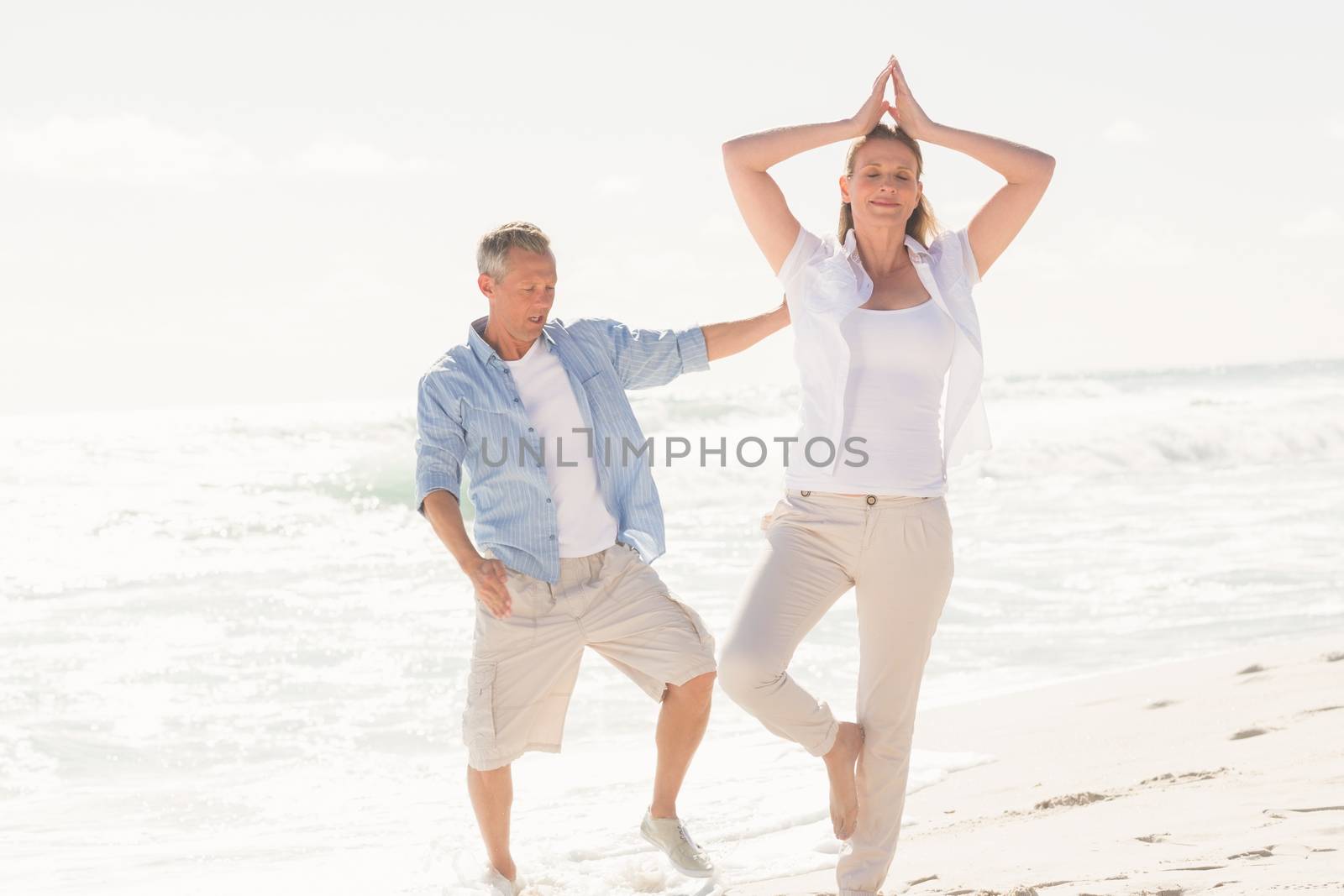 Happy couple doing yoga at the beach