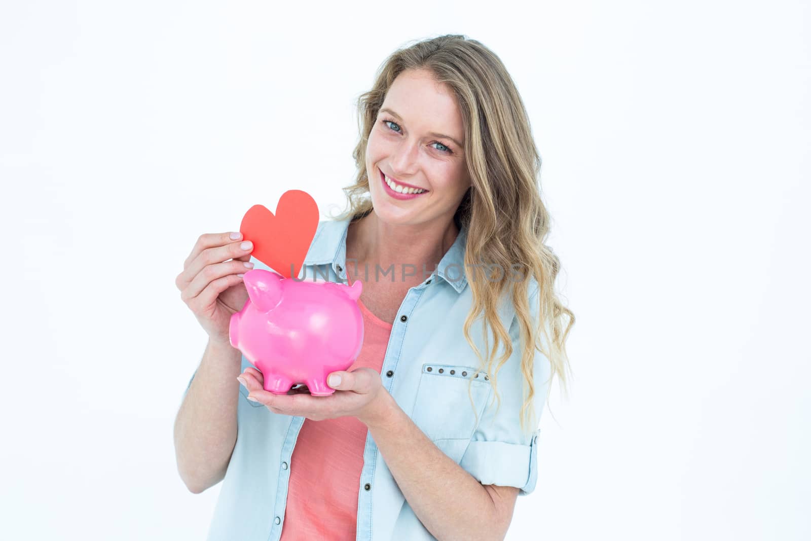 Smiling woman holding piggy bank and red heart on white background 