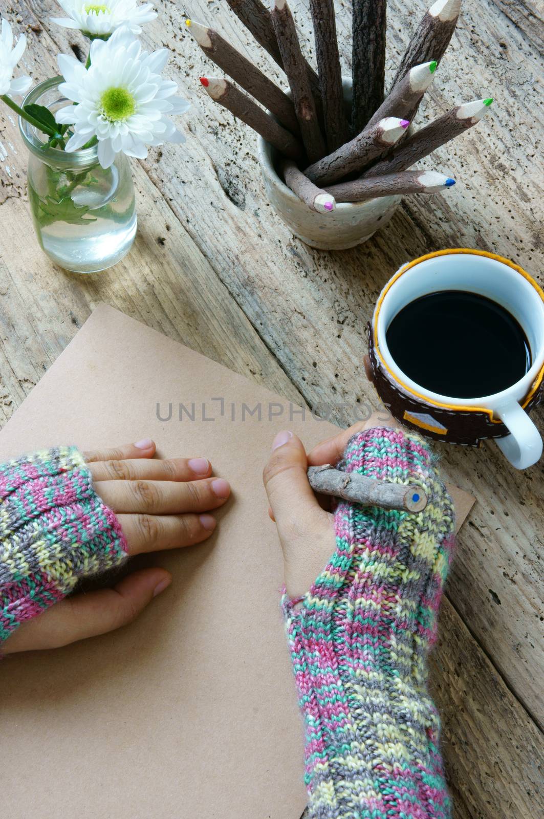 Women hand wear wool gloves in wintertime, writting letter for lover from distant, lonely background in cold day of christmas season, hot coffee cup, flower pot, pencil on wooden background