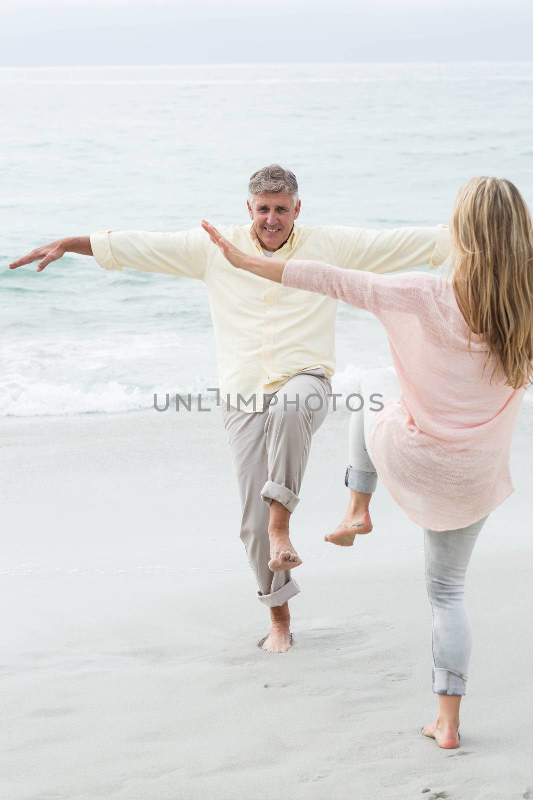 Happy couple doing yoga pose at the beach