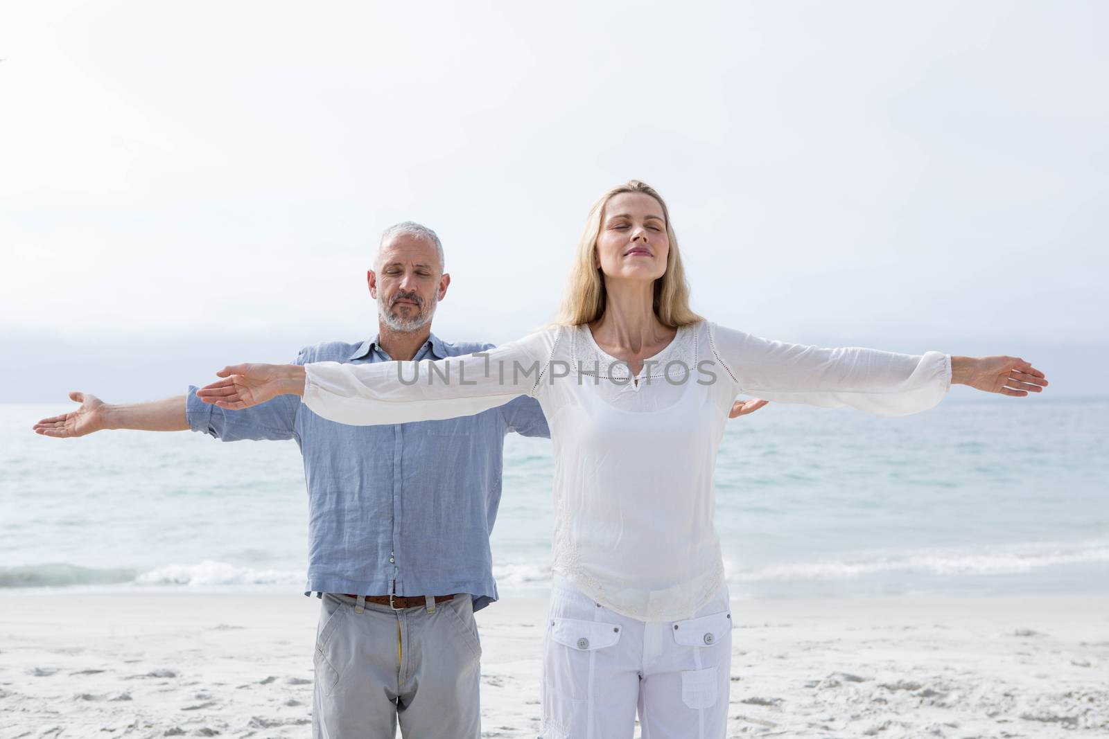 Happy couple doing yoga together at the beach