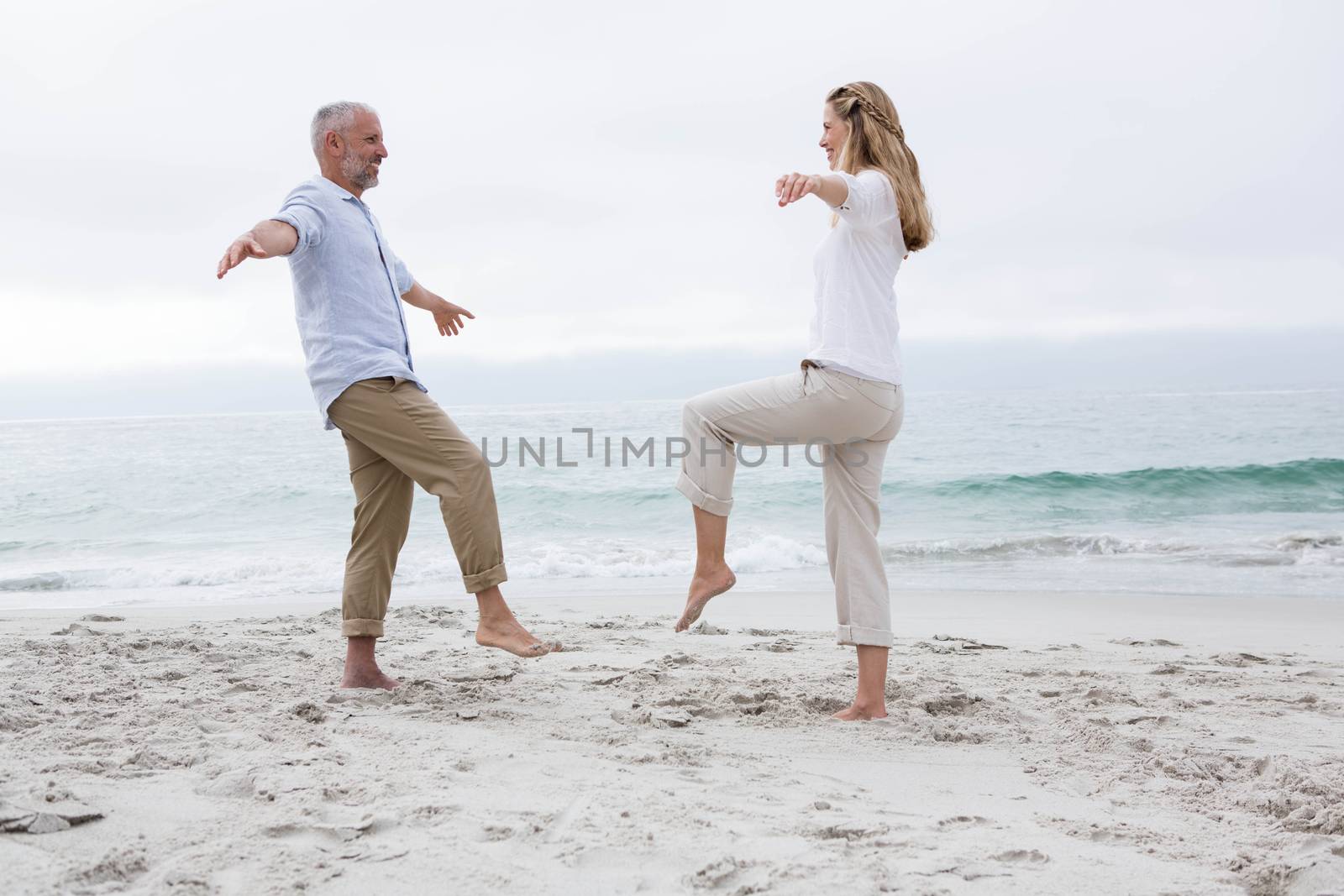 Happy couple doing yoga pose at the beach