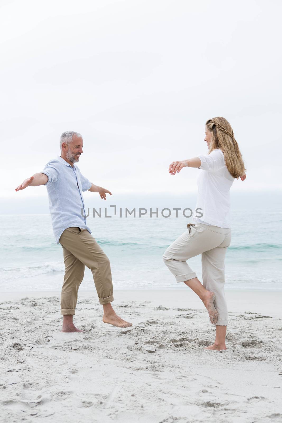 Happy couple doing yoga pose at the beach
