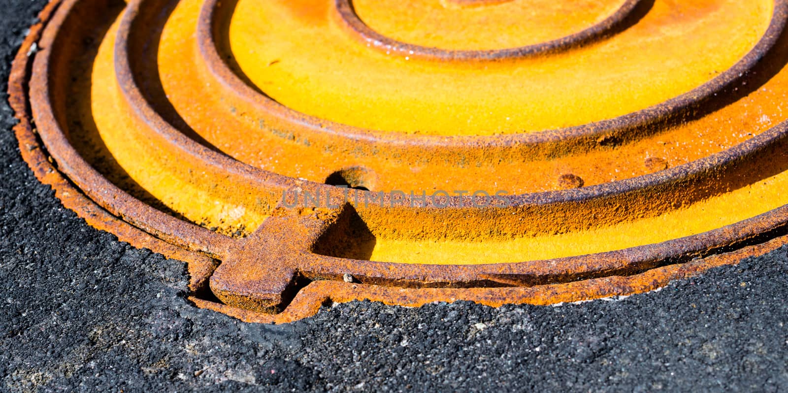 Rusty metal manhole cover in black asphalt surface
