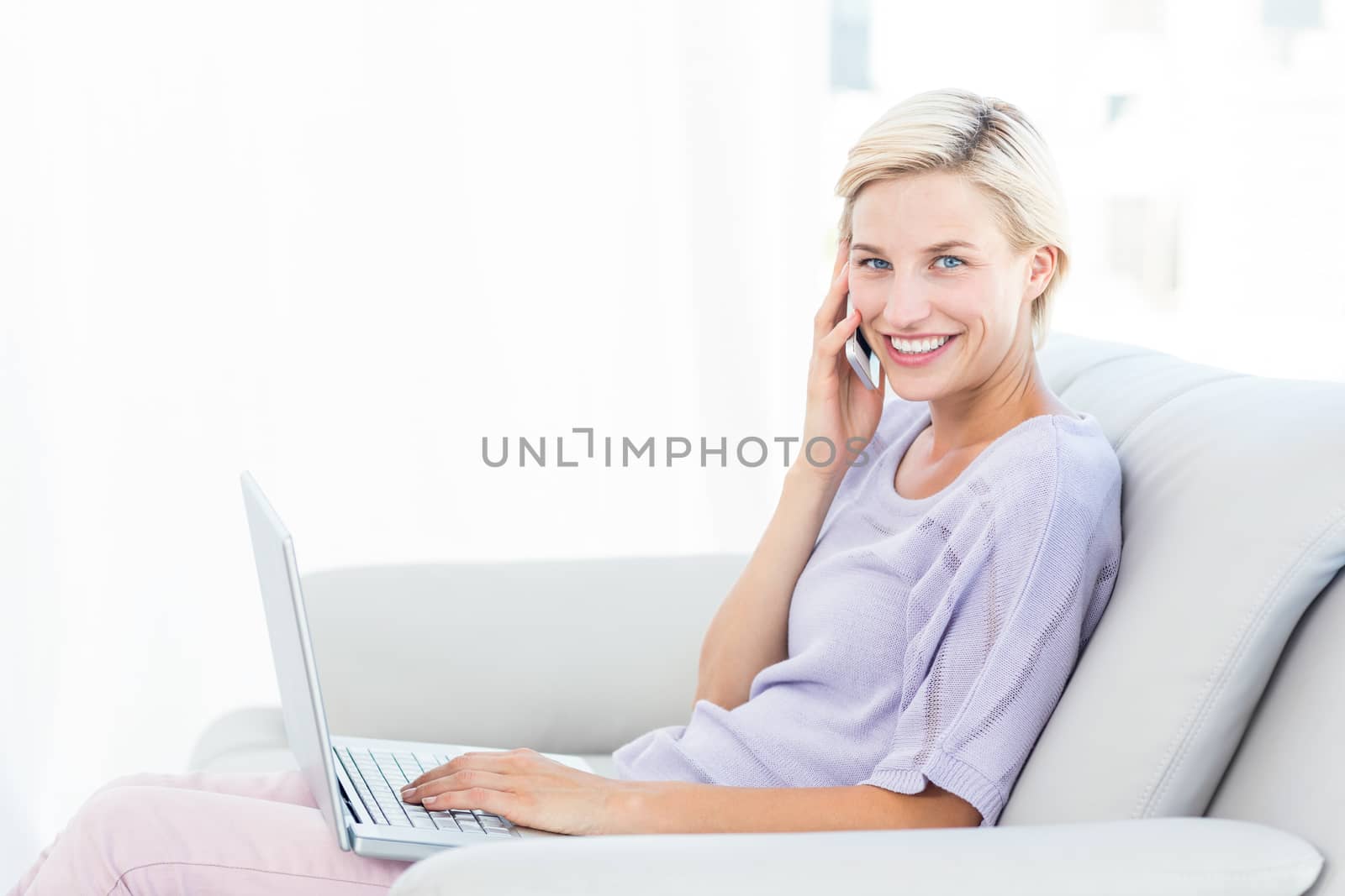Pretty blonde woman calling on the phone and using her laptop by Wavebreakmedia
