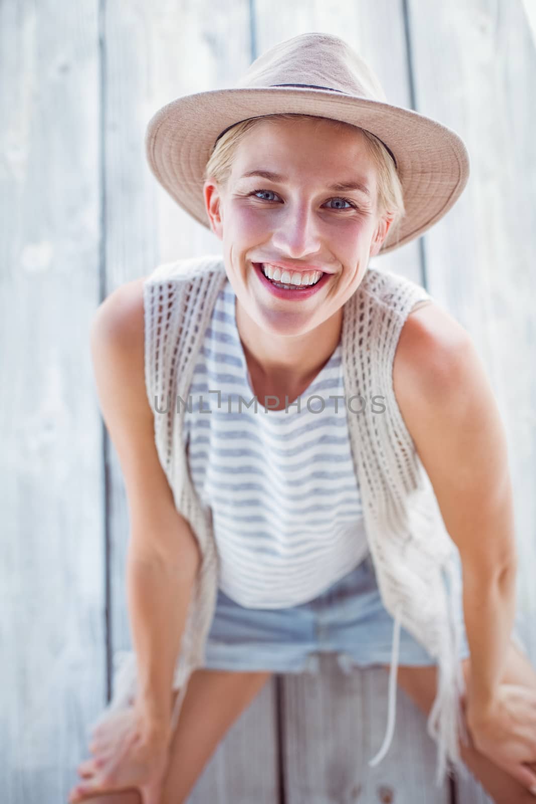 Pretty blonde woman wearing hat and smiling at camera on wooden background