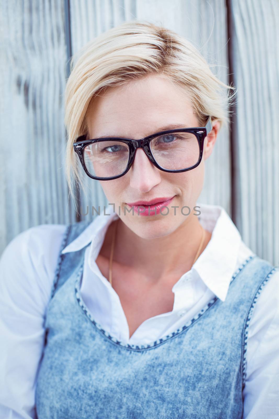 Pretty blonde woman smiling at the camera and wearing hipster glasses in the park