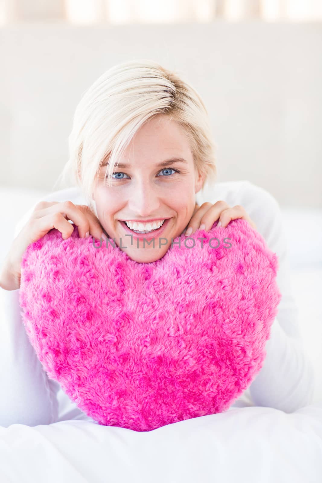 Smiling blonde woman holding heart pillow in the bedroom