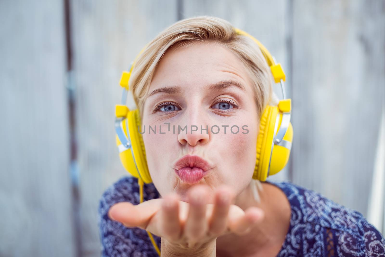 Pretty blonde woman listening music and blowing kiss on wooden background