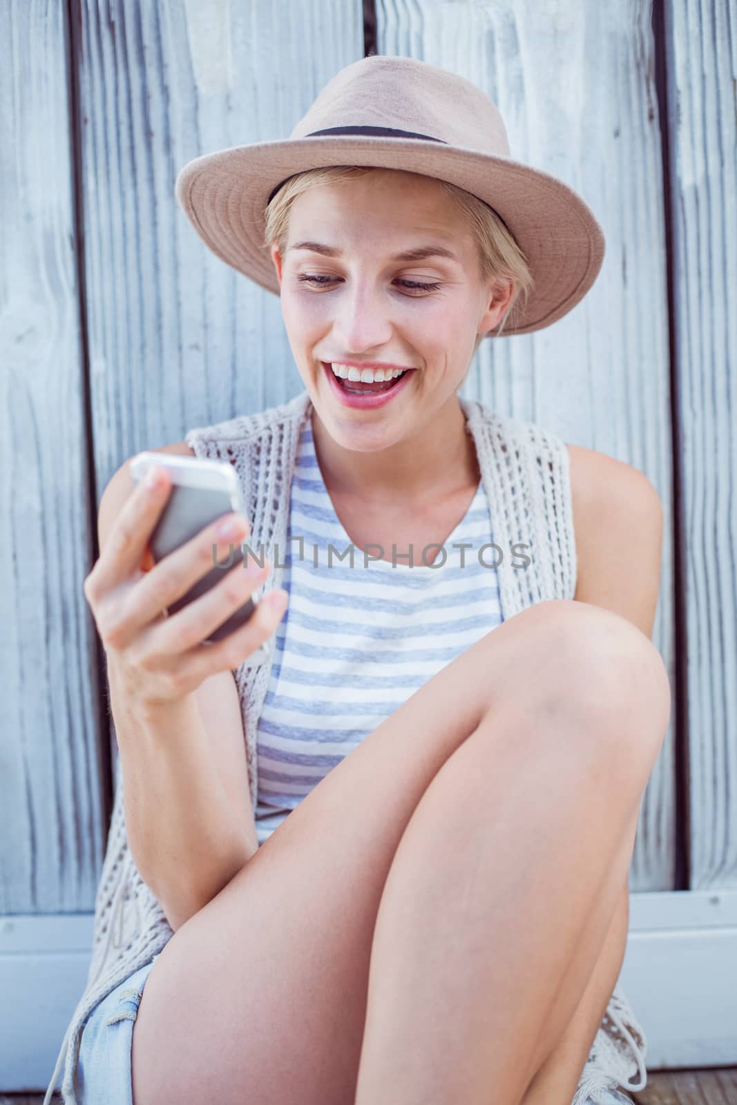 Pretty blonde woman texting with her mobile phone on wooden background 