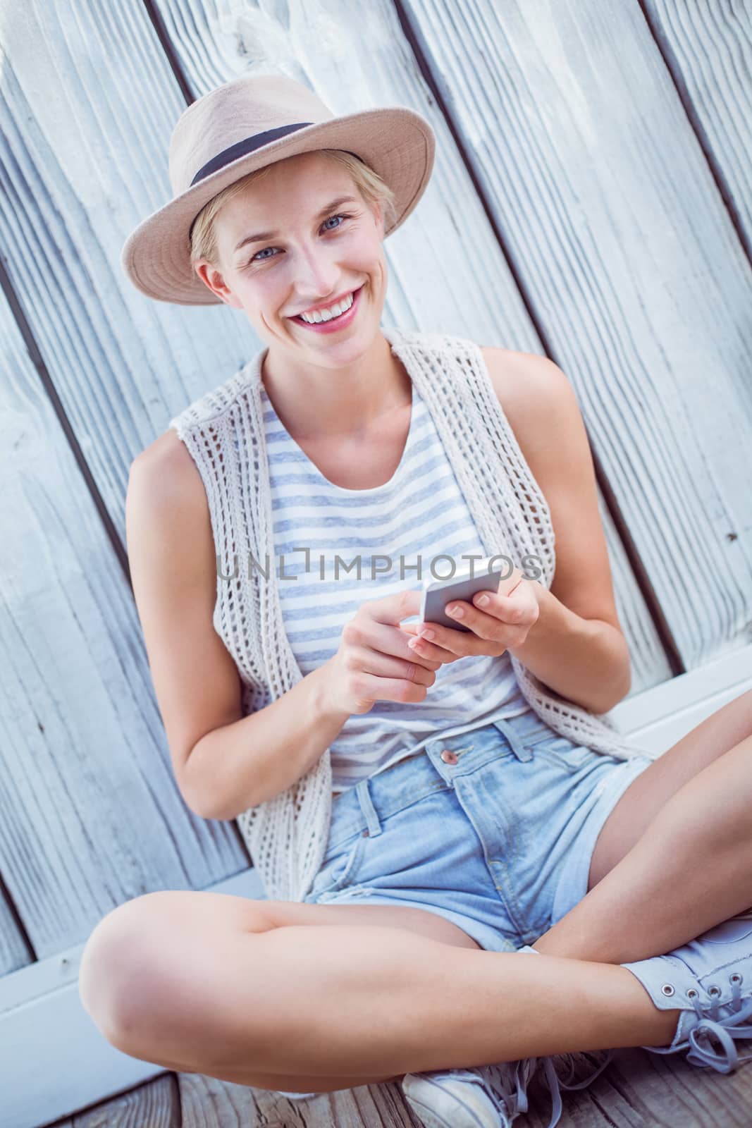 Pretty blonde woman texting with her mobile phone on wooden background 