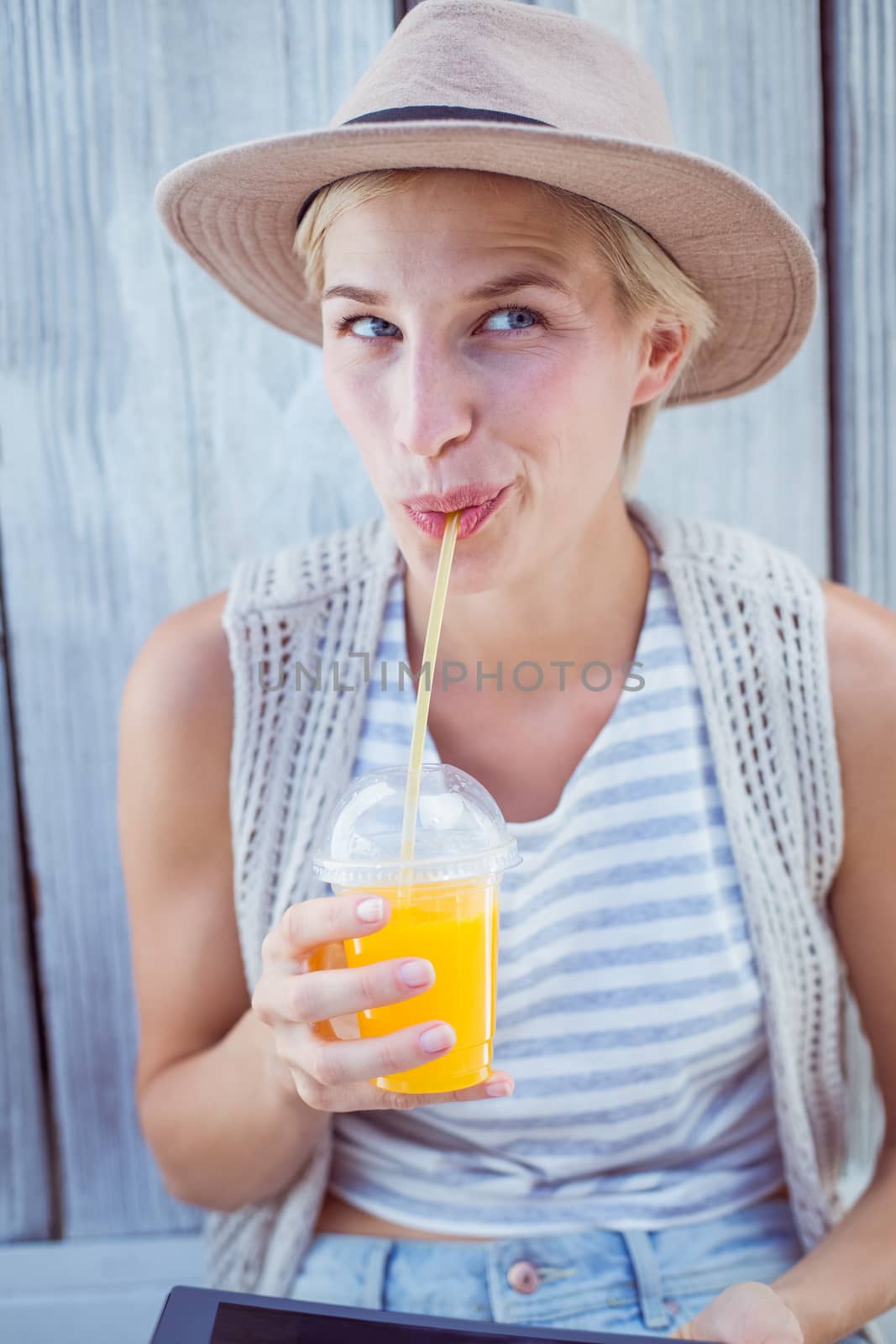 Pretty blonde woman using her tablet and drinking orange juice on wooden background