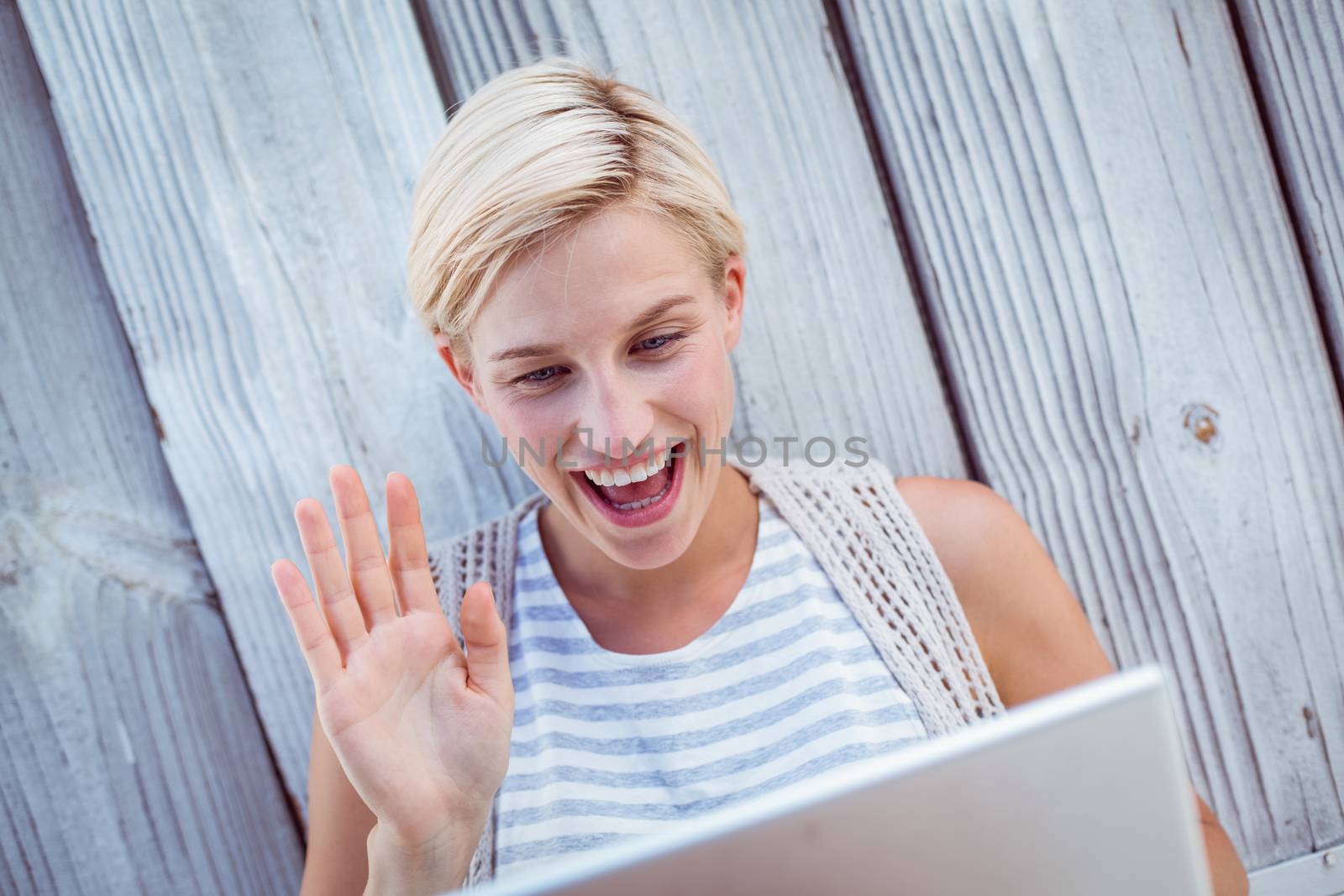 Pretty blonde woman speaking with someone online on wooden background