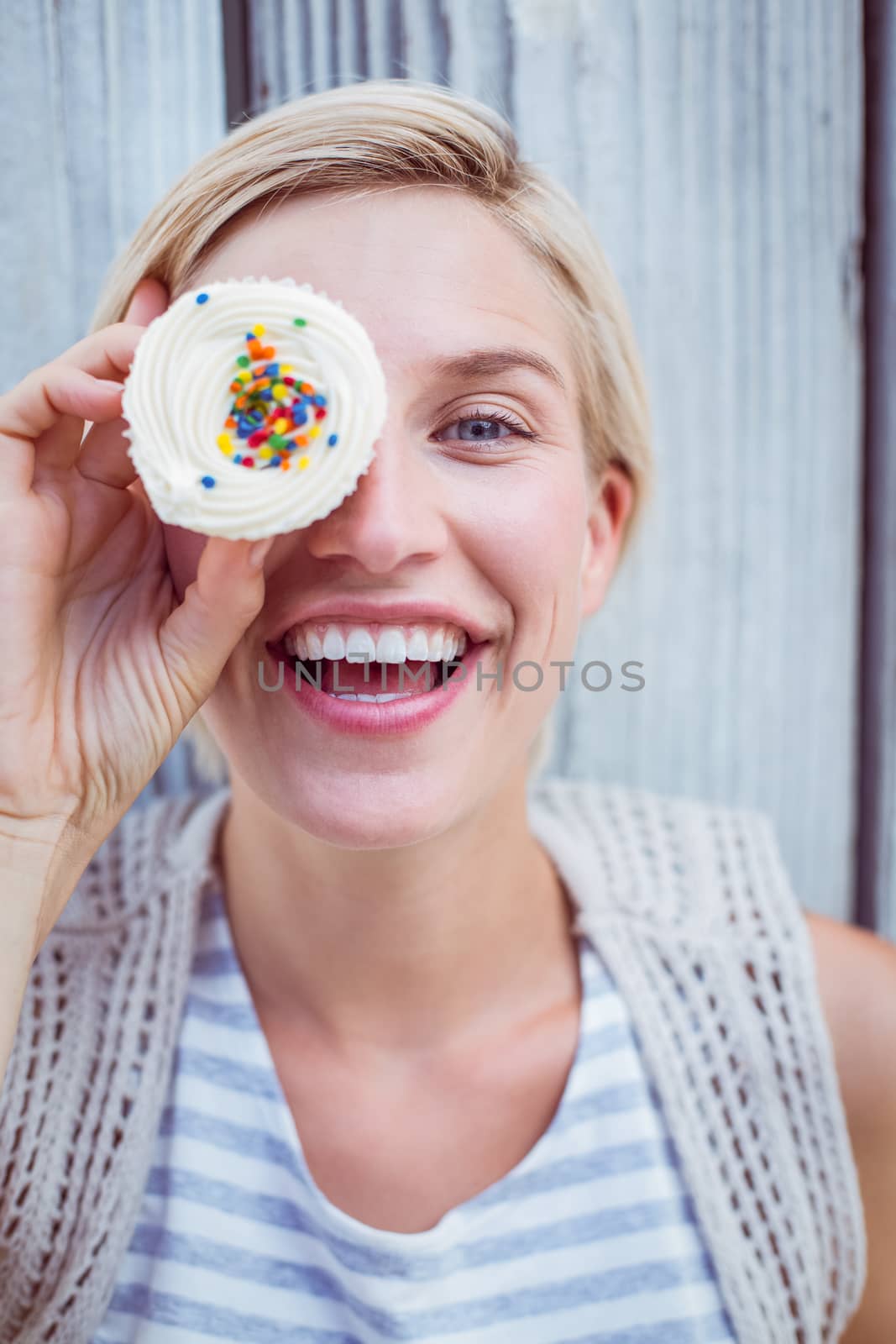 Pretty blonde woman grimacing with cupcake on wooden background