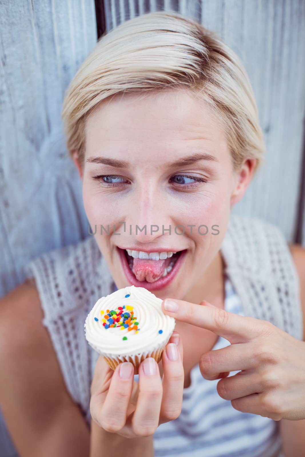 Pretty blonde woman tasting the cupcake on wooden background