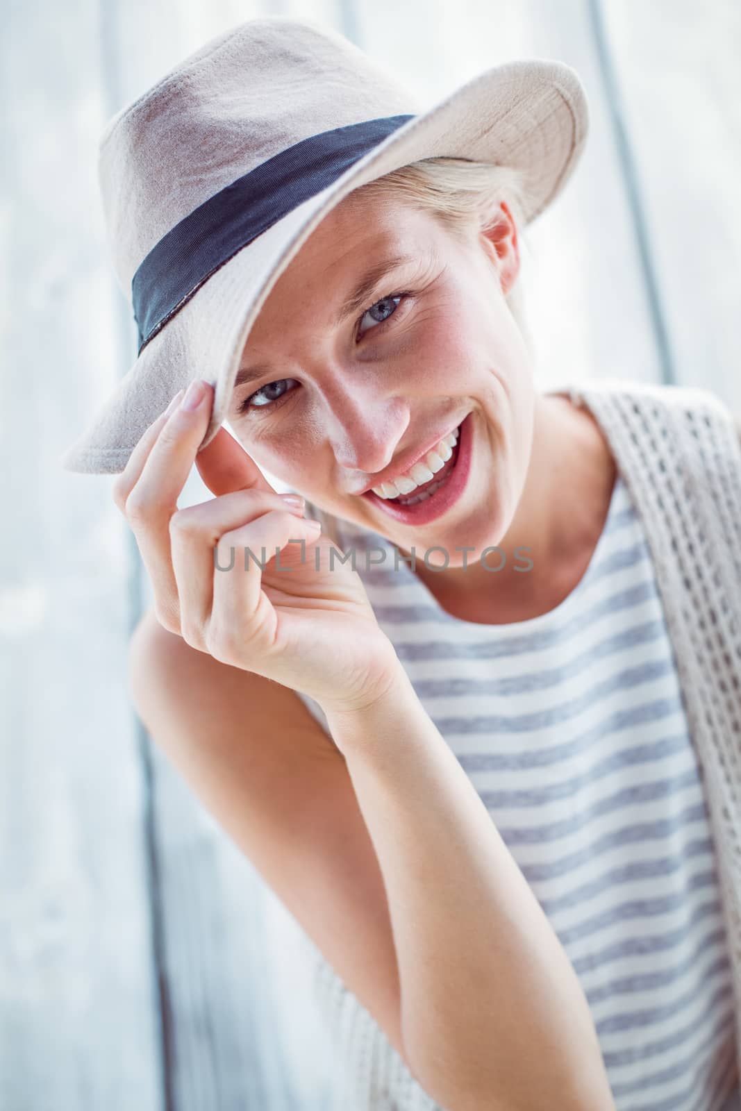 Pretty blonde woman wearing hat and smiling at camera on wooden background