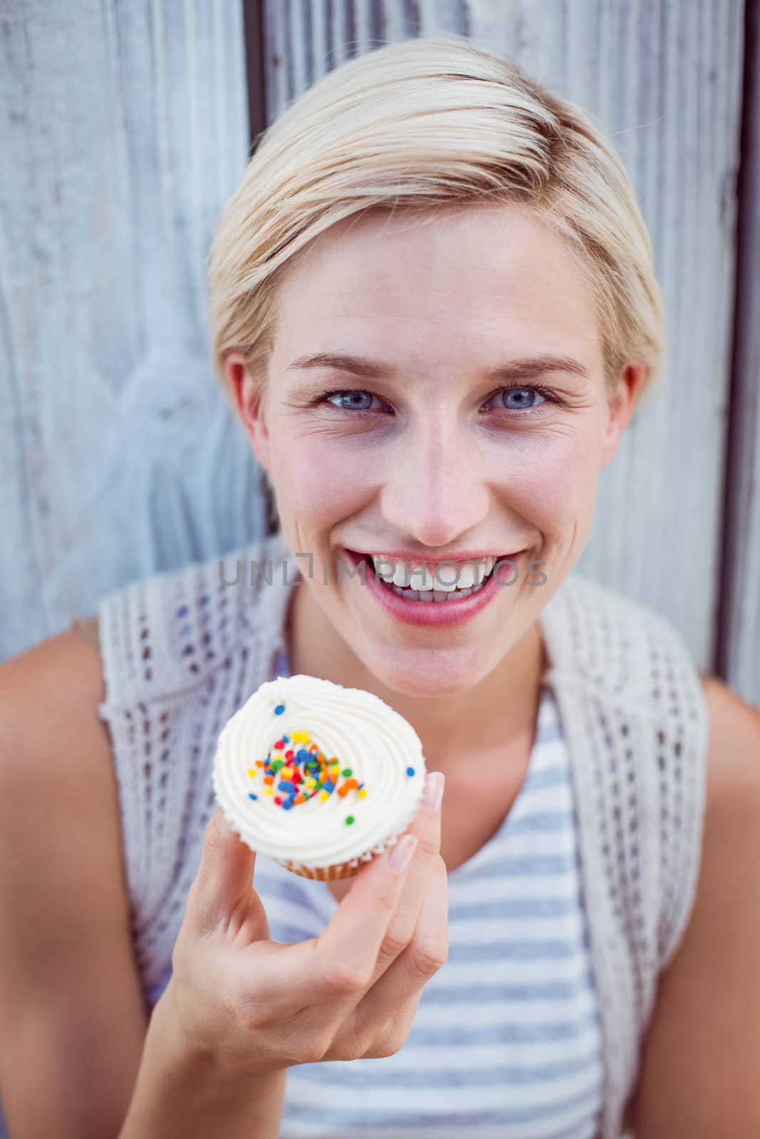 Pretty blonde woman holding cupcake on wooden background